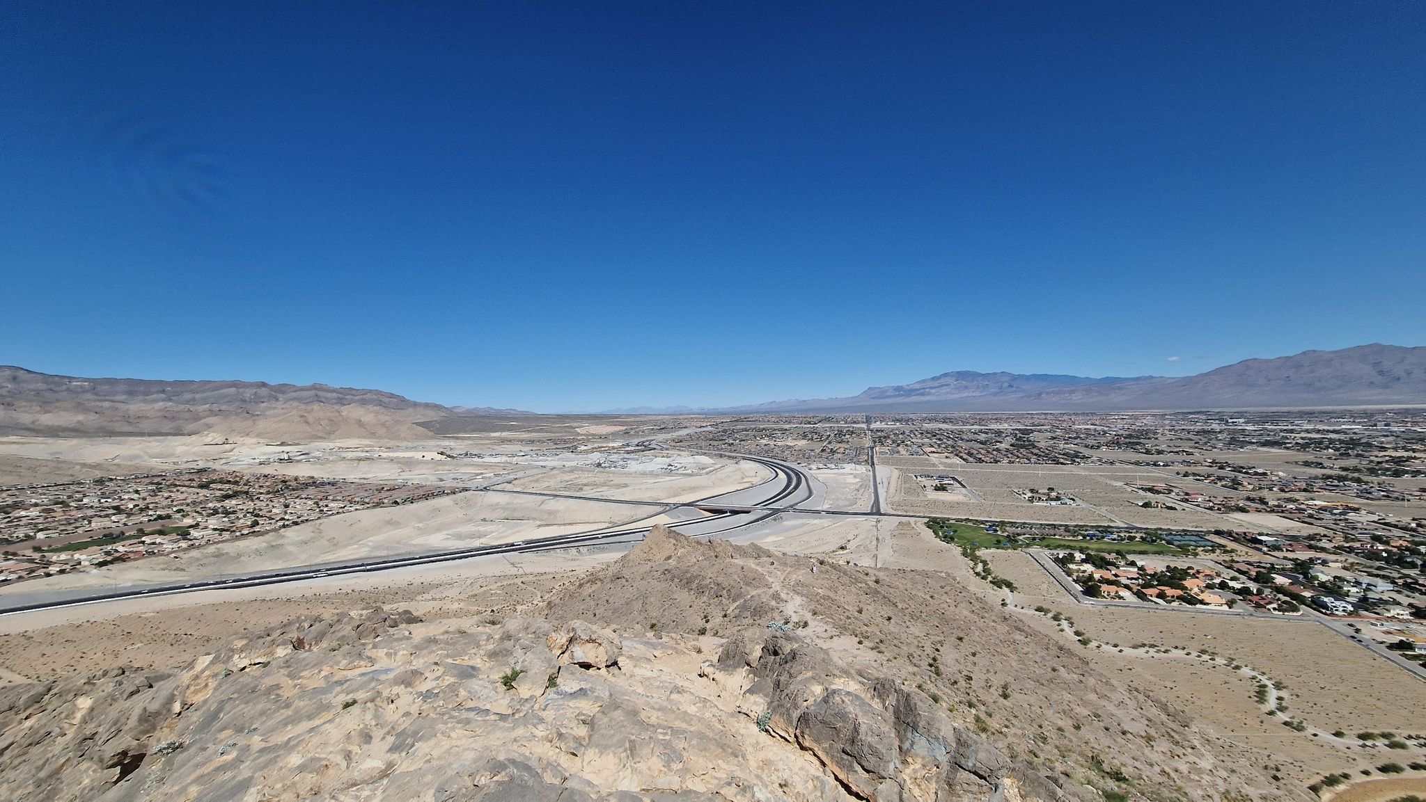 Elevated view of a desert highway winding through a valley with distant mountains. - Lone Mountain Loop