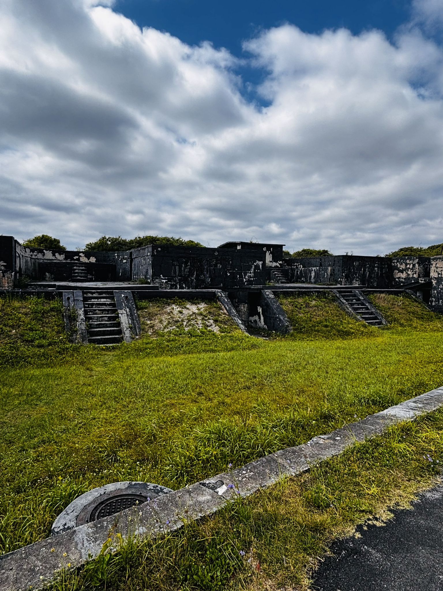 Old concrete fortifications with grassy slopes under a cloudy sky. - Battery Trueman – Battery Payne loop from Sugar Bowl Protected Area