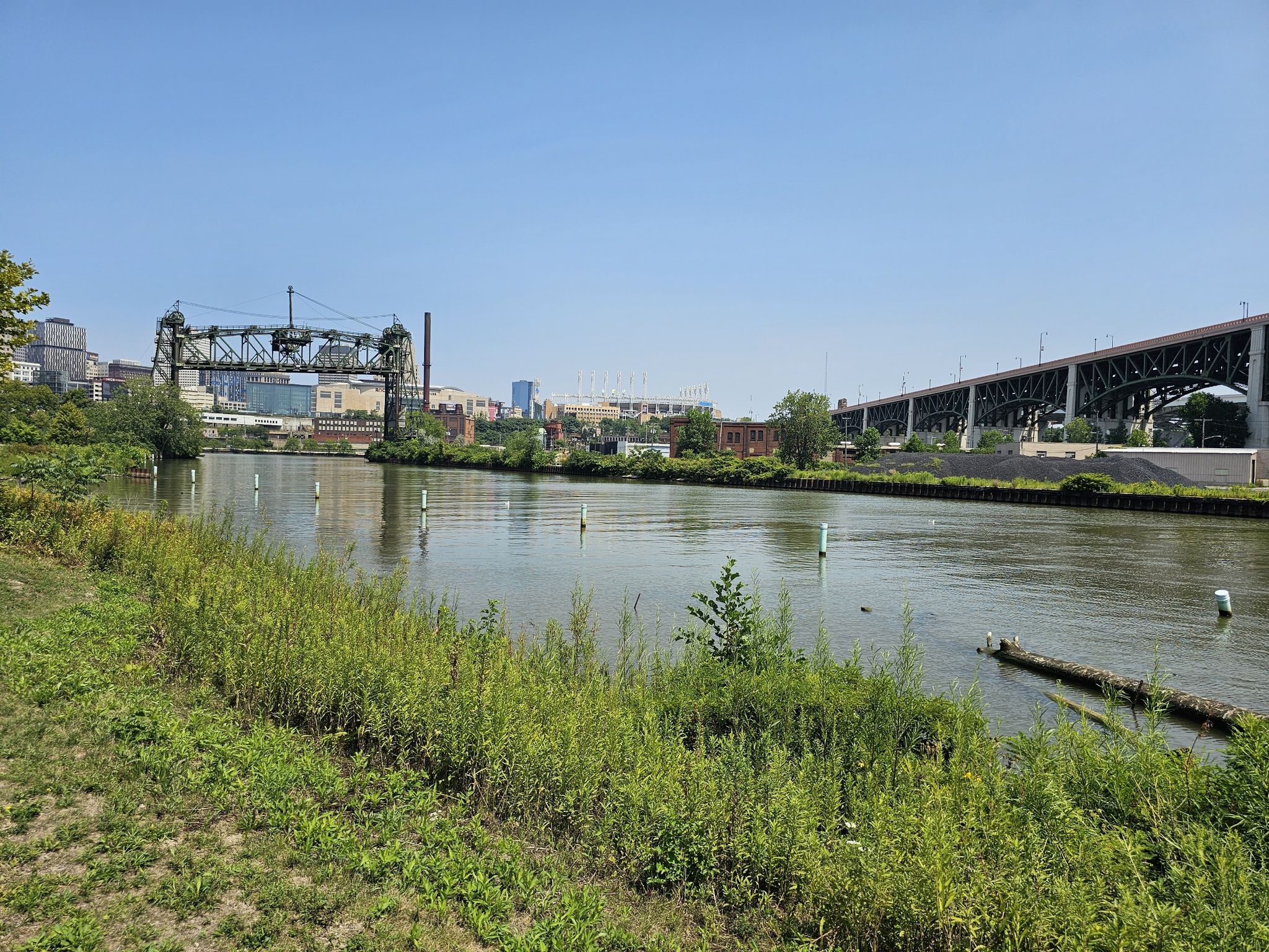 Wide river with green banks, industrial bridges, and city buildings under clear sky. - Ohio and Erie Canal Towpath: Scranton Flats
