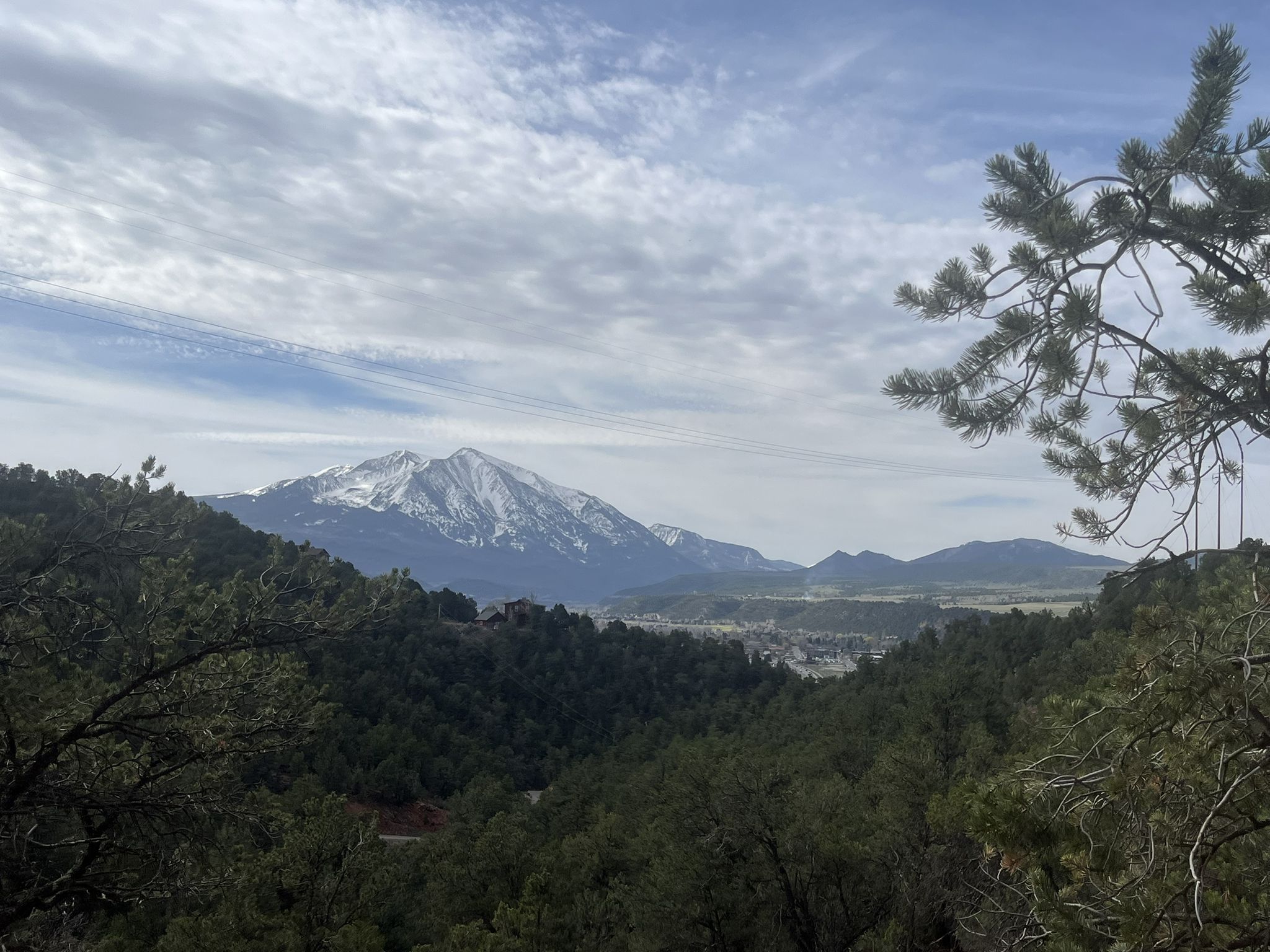 Distant snow-capped mountain and valley under a cloudy sky, framed by trees. - Mushroom Rock loop
