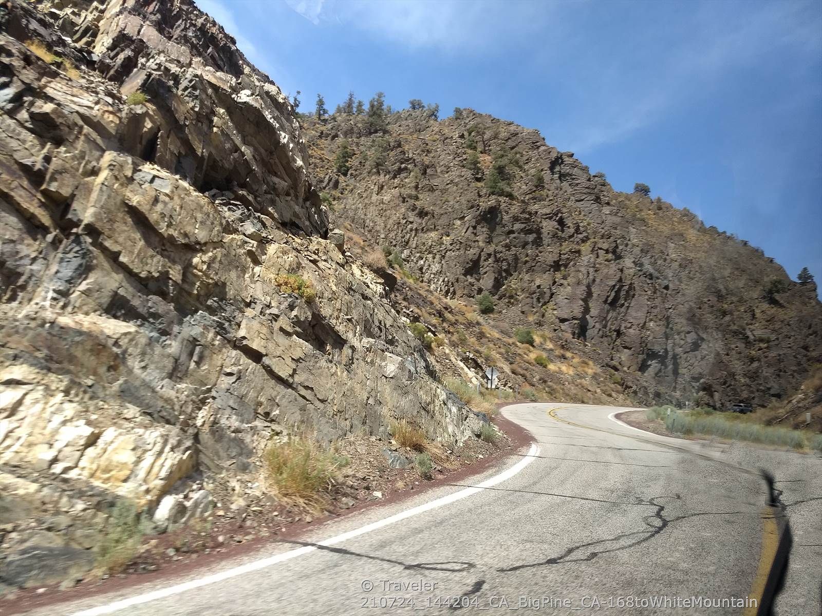 Winding paved road through a steep, rocky mountain pass on a sunny day. - Schulman Grove Visitor Center via White Mountain Road