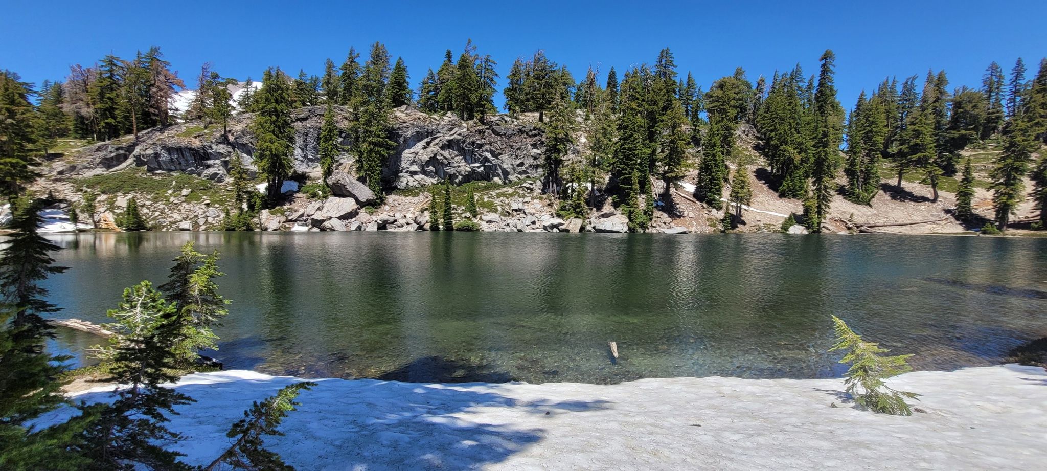 A clear mountain lake with snow on the shore, surrounded by pine trees. - Terrace, Shadow, and Cliff Lakes