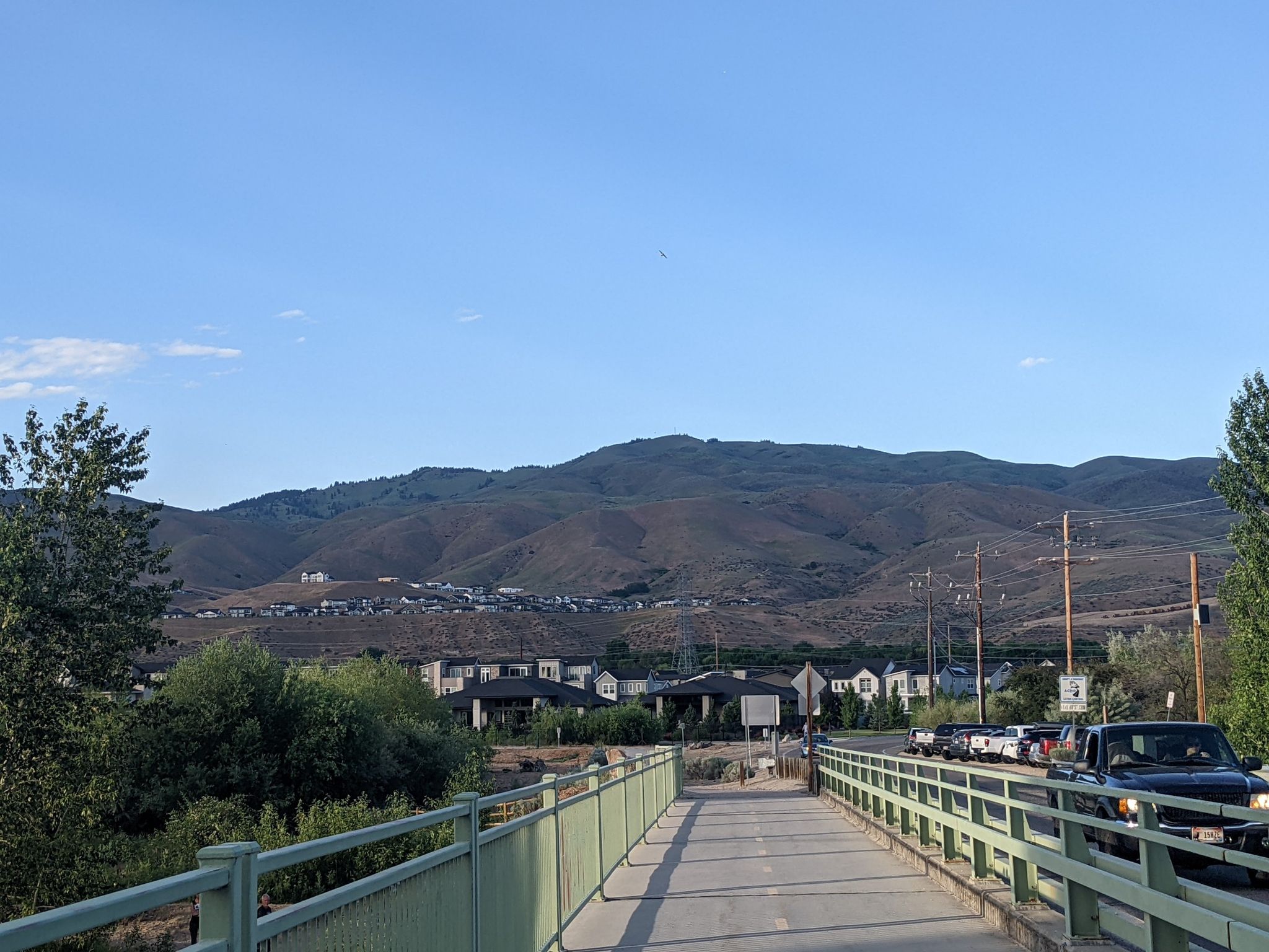 Bridge leading to houses and mountains under a clear daytime sky. - Boise River Greenbelt