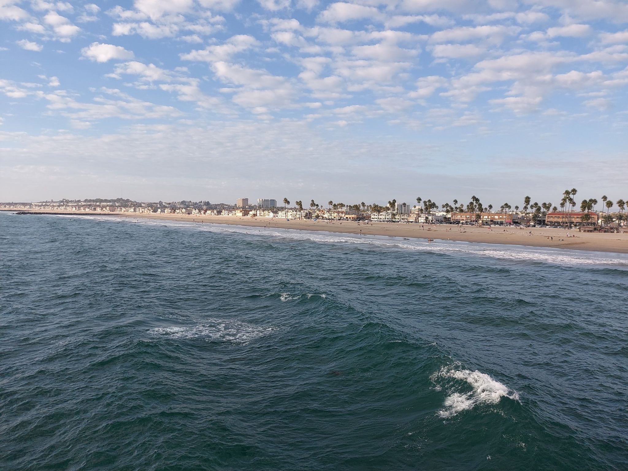 Wide ocean view with waves, a distant sandy beach, and buildings. - Newport Pier to Balboa Pier