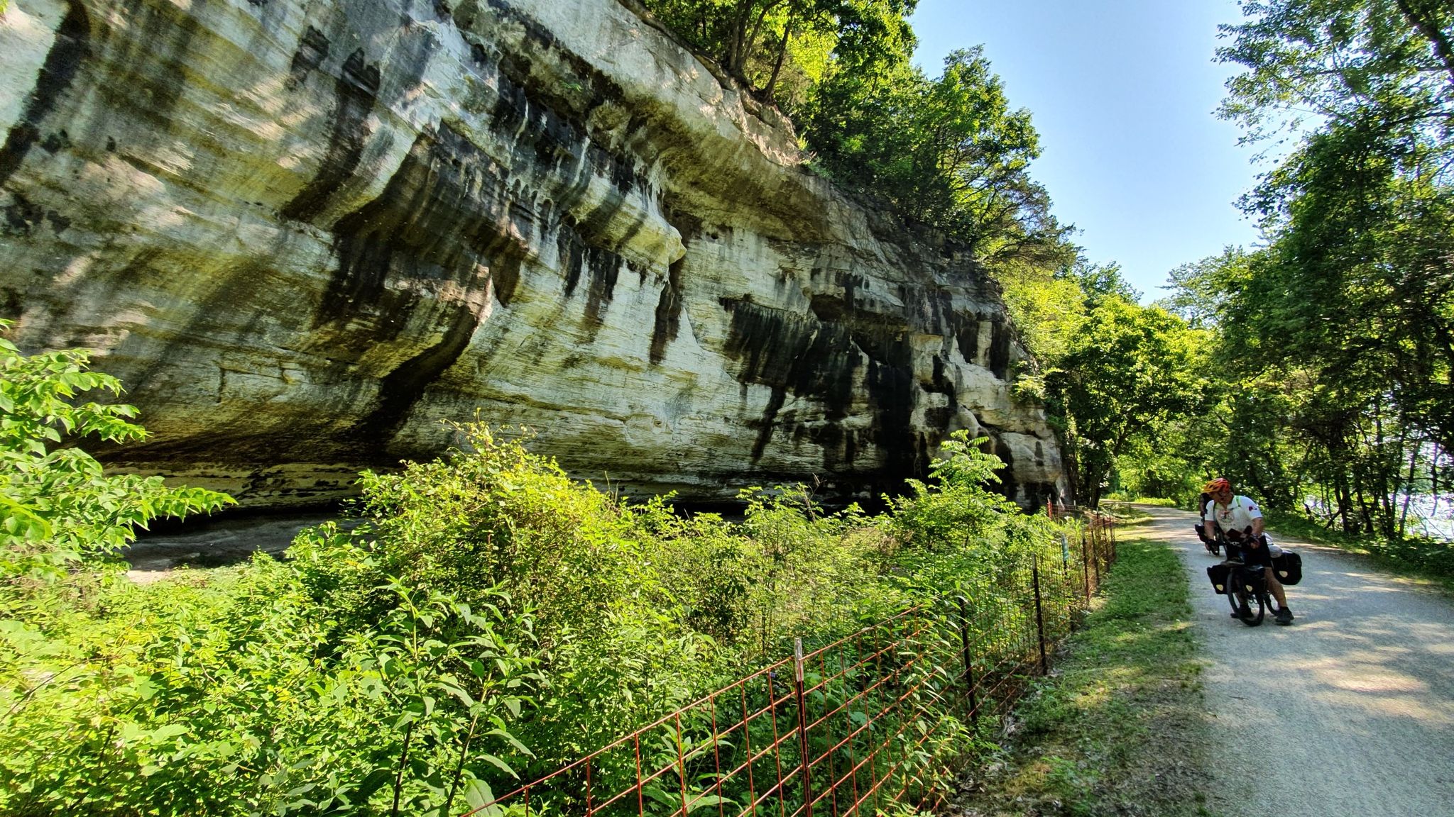 Cyclist on a dirt path next to a large, textured rock cliff, sunny. - Hogsback Trail Loop
