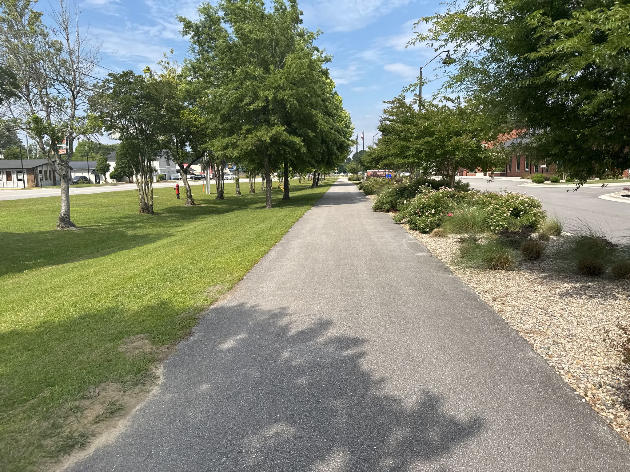 Paved path with trees and grass under bright sunny skies. - Rails to Trails Greenway – Lejeune Memorial Gardens loop from Brynnwood Townhouses