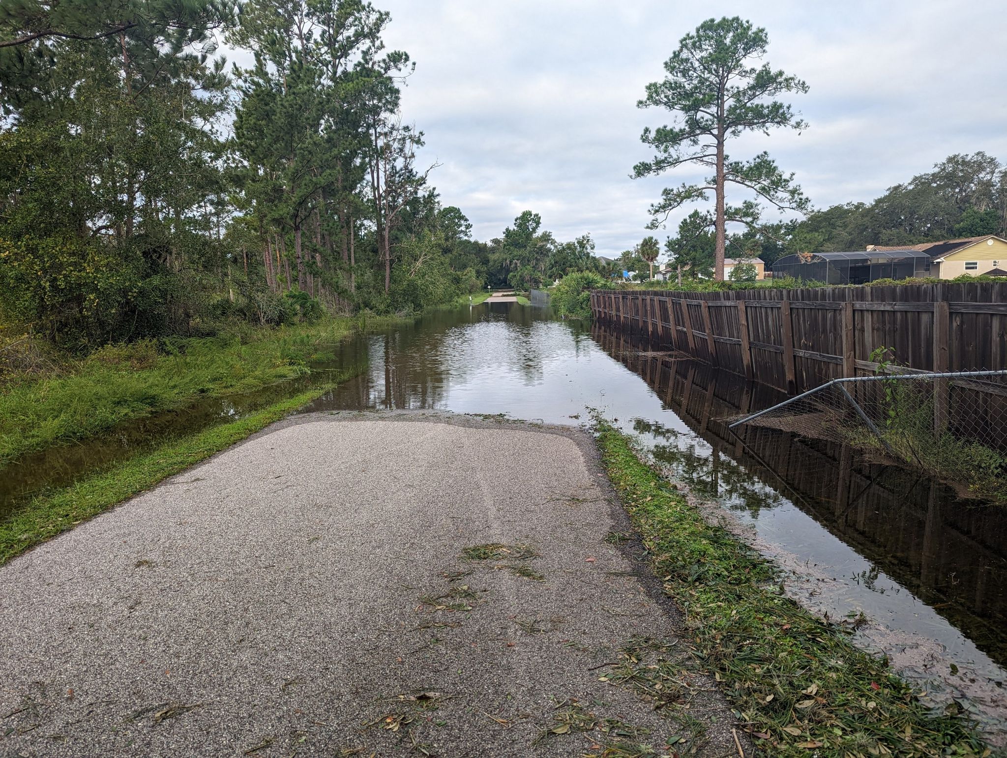 Overcast view of a flooded paved road next to a wooden fence. - Trues Lake loop from Heathrow