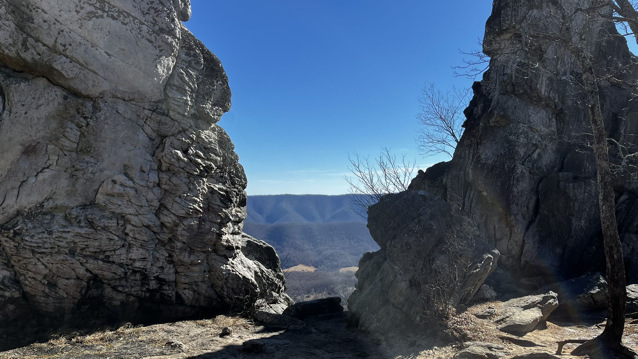 A scenic view through a rock gap to distant mountains under a clear blue sky. - Dragon's Tooth From Miller Cove Road