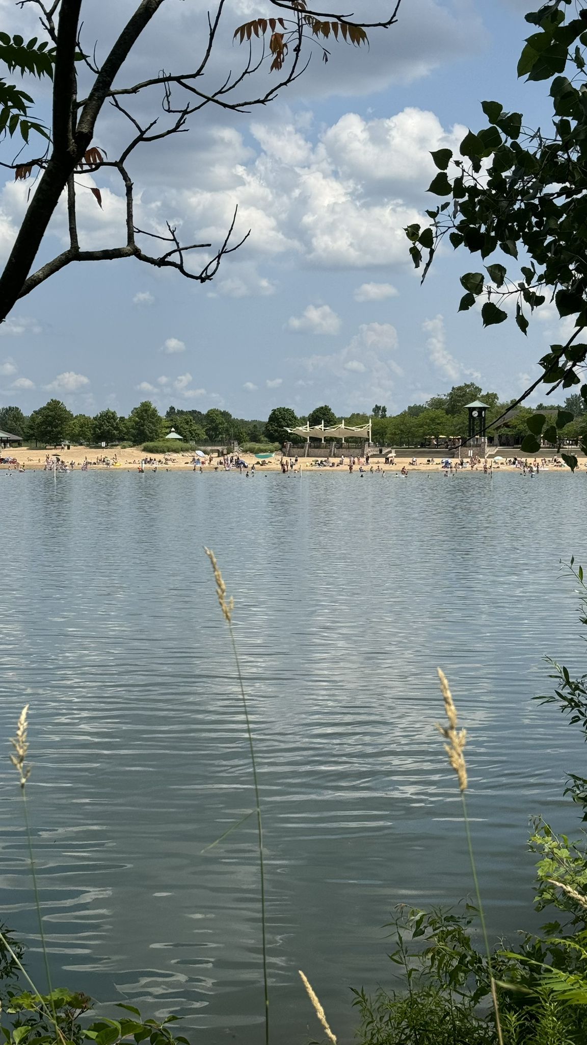 Calm lake with a distant sandy beach full of people under a bright, cloudy sky. - Lake Leota and Millennium Park Lake Loop
