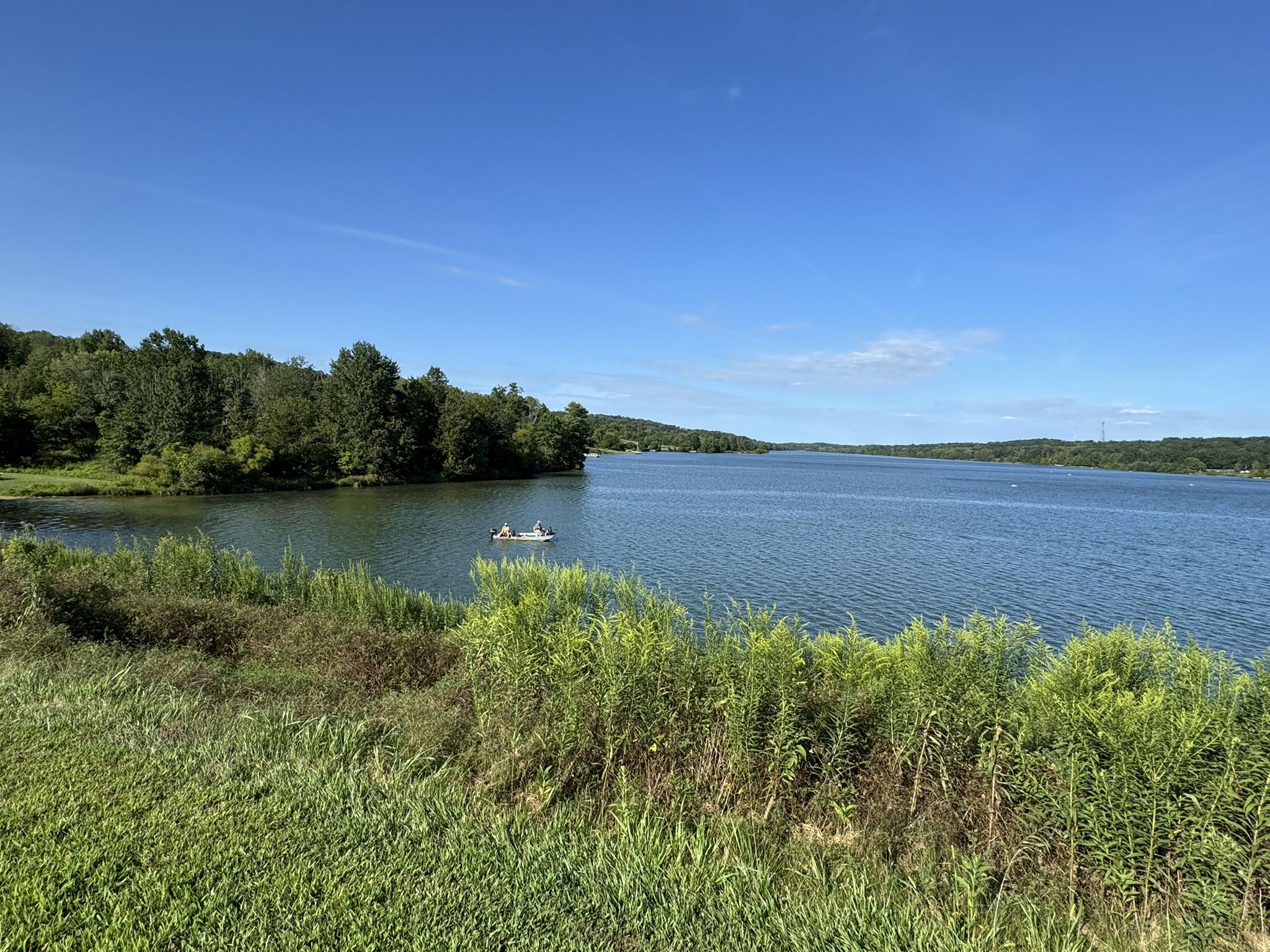 Sunny day over a wide lake with forested shores and a small boat. - Lake Galena – Peace Valley Park loop from National Shrine of Our Lady of Czestochowa