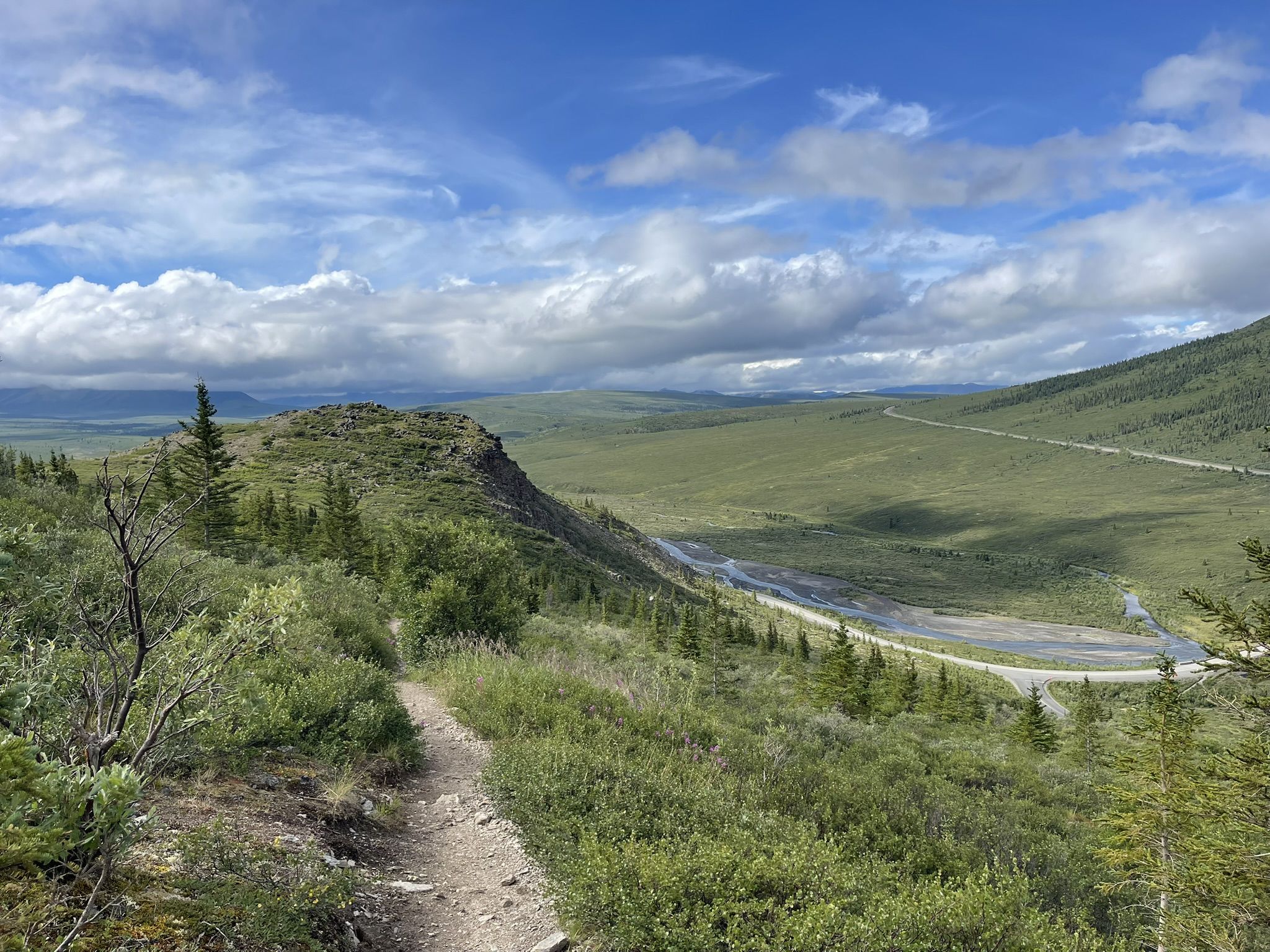 Dirt path through green hills, with a river and road in the distance. - Savage Alpine Trail