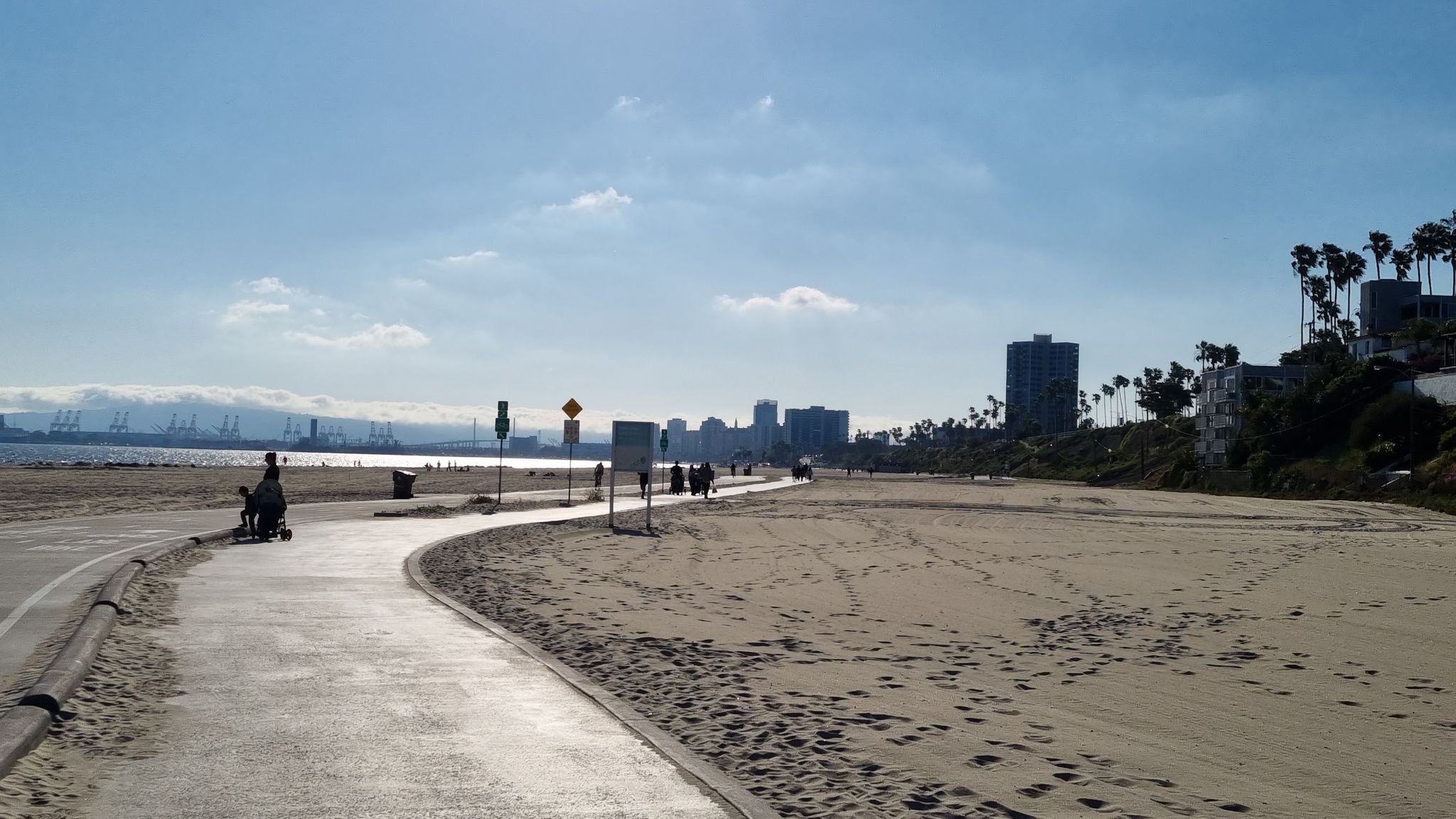 Paved beach path with people walking, city skyline, and ocean under sunny skies. - Beautiful Beach Bike Path – Long Beach City Beach loop from Naples Islands