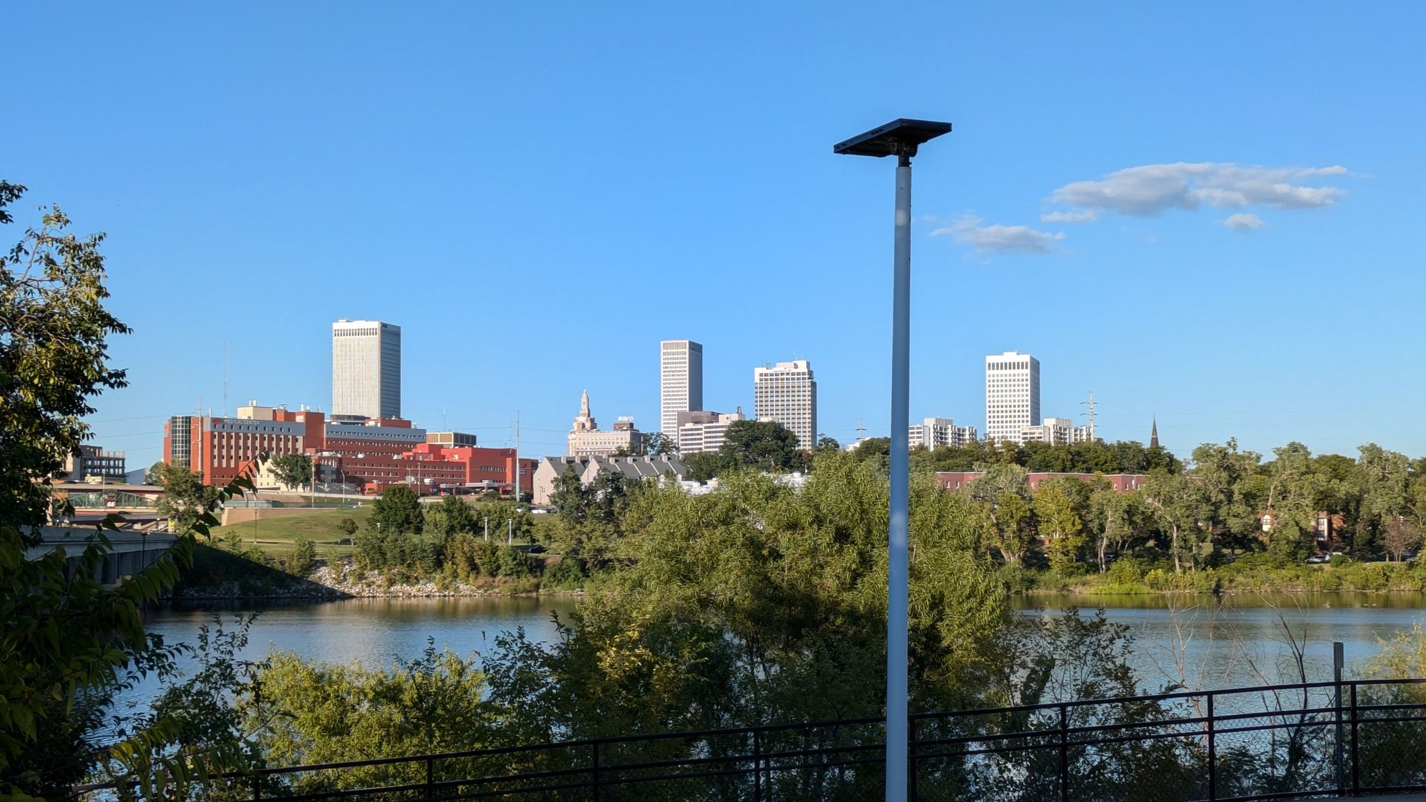 Distant city skyline with tall buildings across a river, framed by green trees. - Route 66 to Sapula