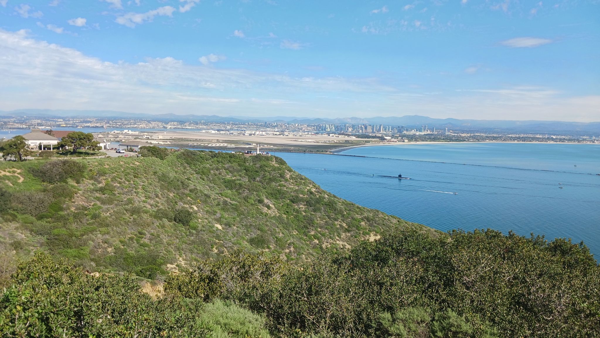 Bright day overlooking a bay, distant city, and green coastal hills. - Bayside Trail