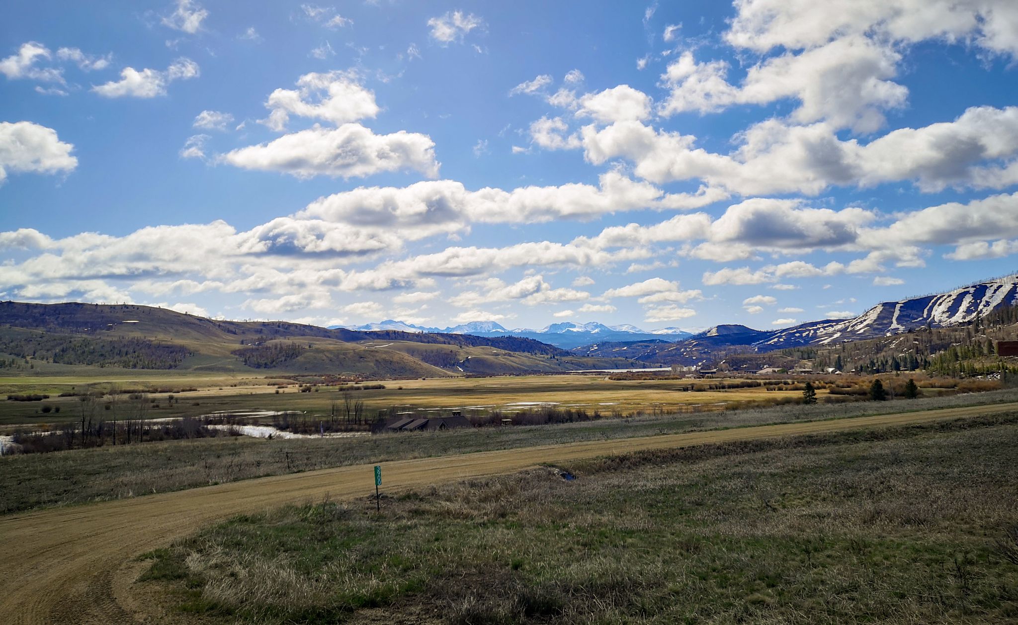 Sunny valley with a river, distant mountains, and a dirt road. - TransAmerica Trail (Colorado)