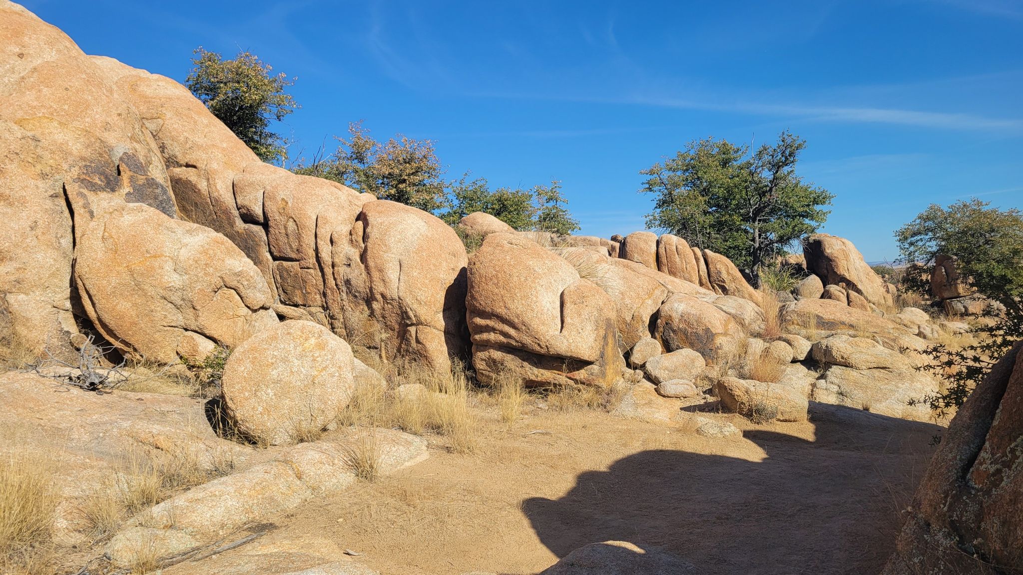 Sunny dirt path through large, smooth rock formations and dry brush. - Constellation Trails Memorial loop from Phippen Museum of Western Art