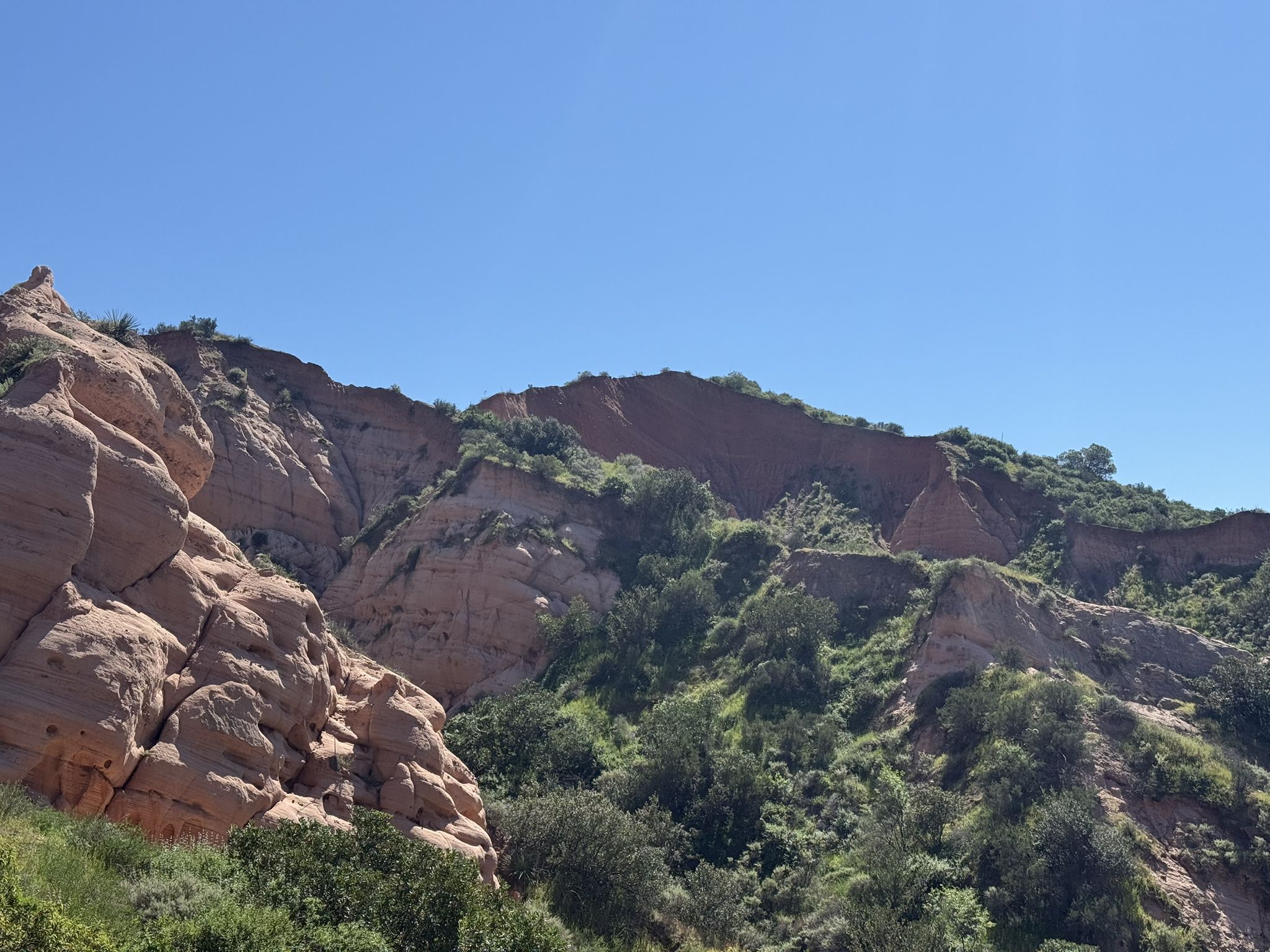 Sunny view of rugged, eroded hillsides with green scrub under a clear sky. - Reynolds Bench – Whiting Ranch Wilderness Park loop from Saddleback Church