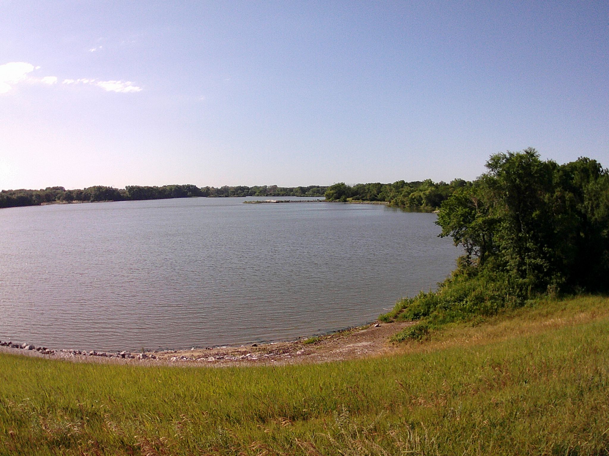 Wide view of a calm lake surrounded by green trees under a clear sky. - South Rock Island Trail – Pioneers Park loop from The Ridge