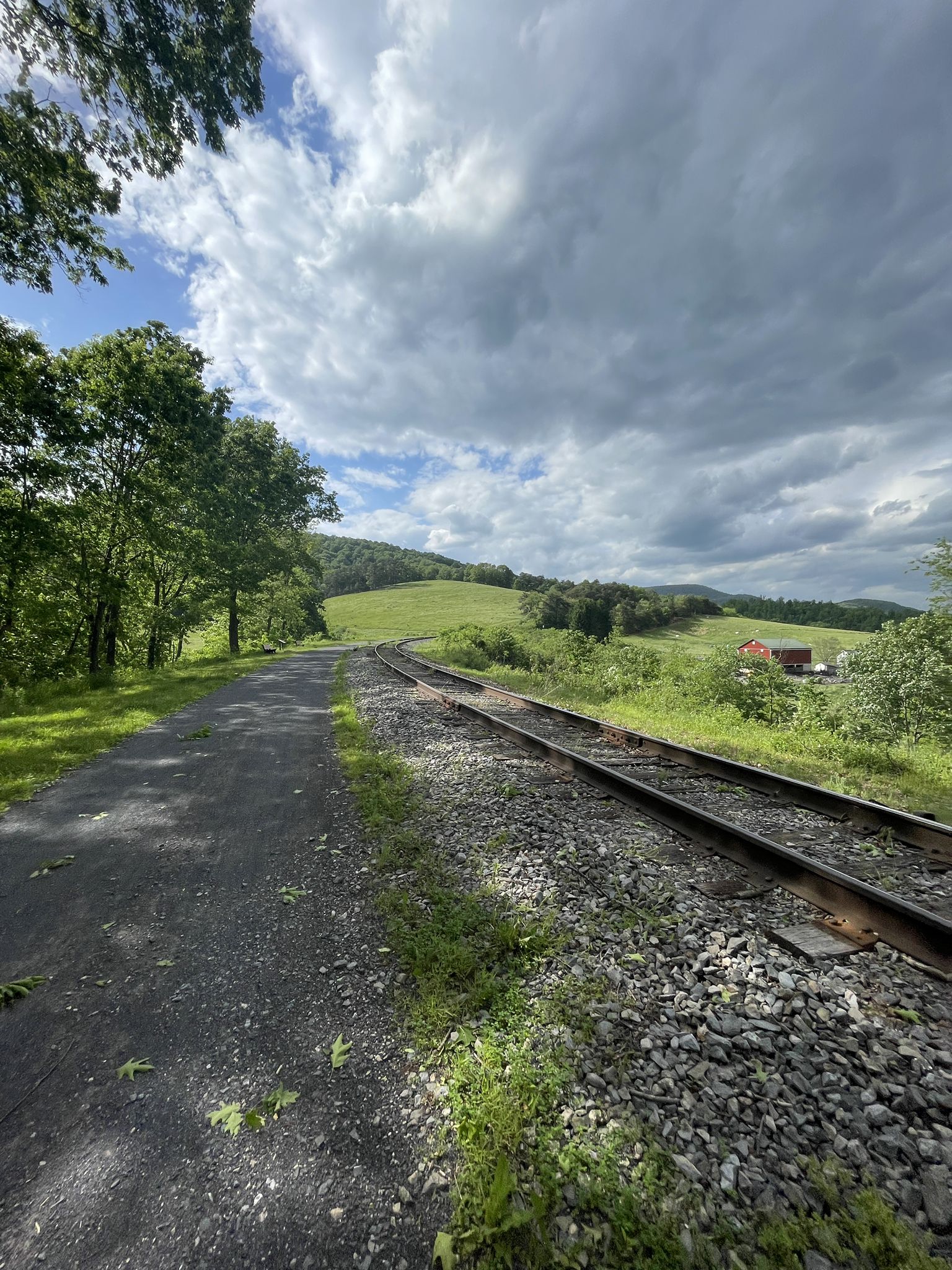 Train tracks run alongside a gravel path, leading to green hills. - Helmstetter’s Curve – Brush Tunnel loop from La Vale