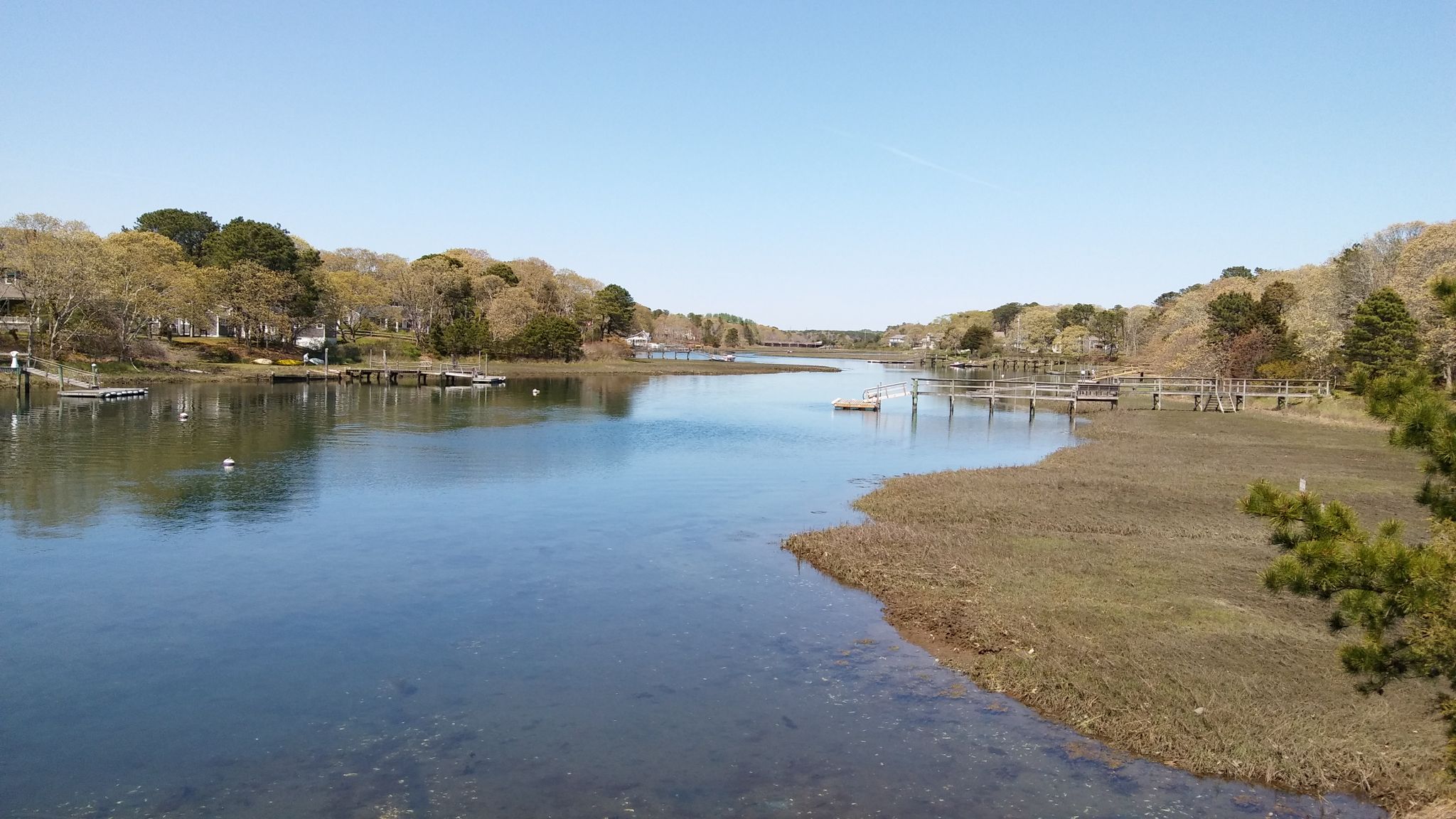 Wide, calm river with forested banks, docks, and a clear blue sky. - View of Wychmere Harbor – Allen Harbor loop from The Twinefield