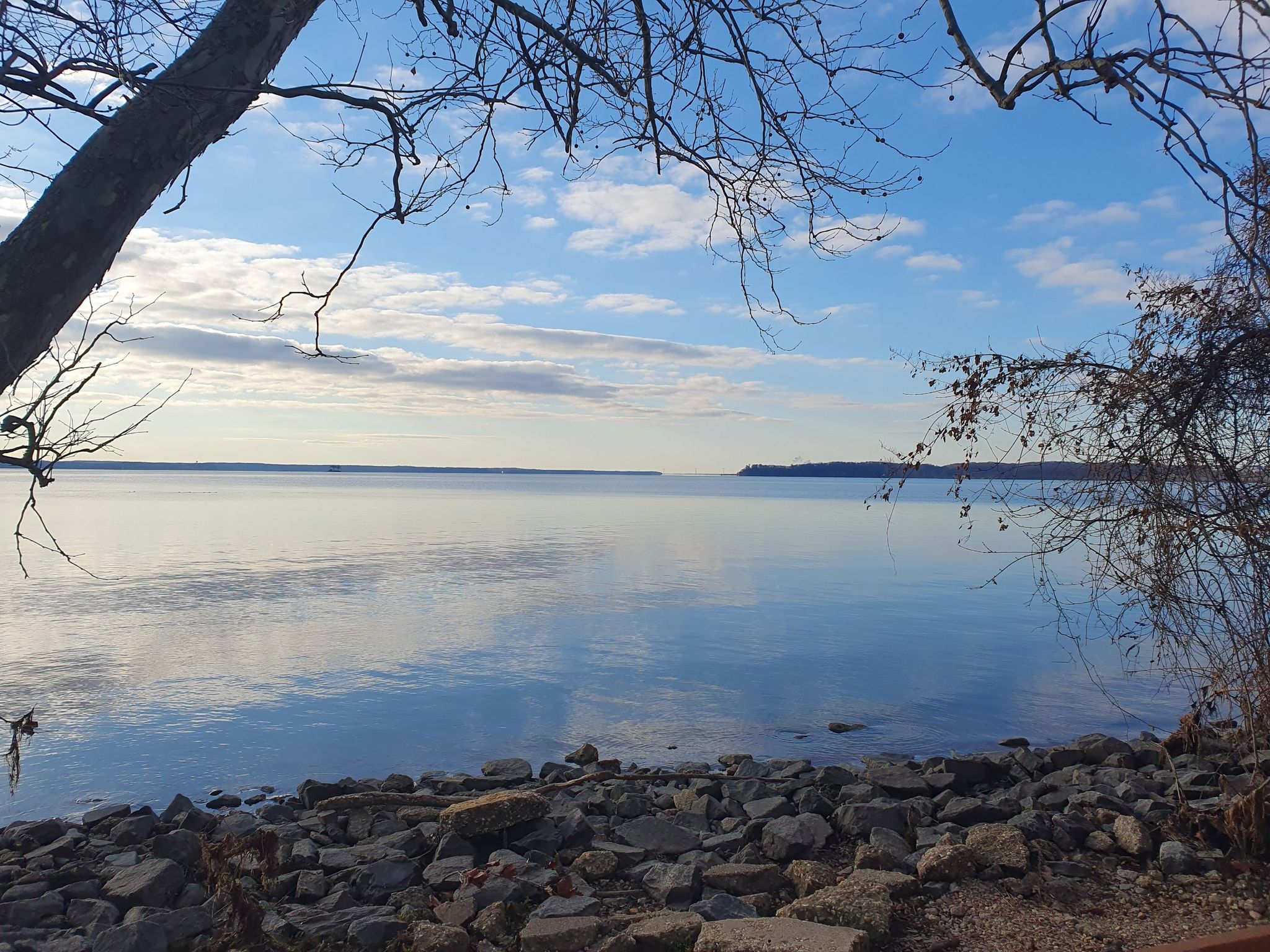 Calm water with a rocky shore and distant land under a blue sky. - Easy Road and Deephole Point Road Loop