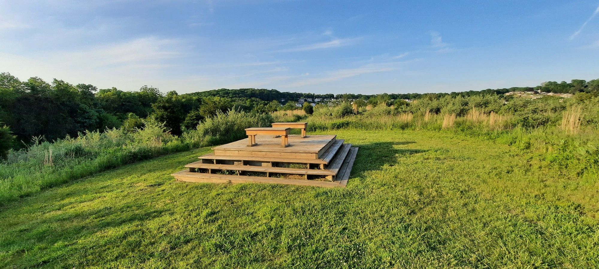 Wooden platform and benches on a grassy hill under a bright blue sky. - Richard Nixon Park Loop