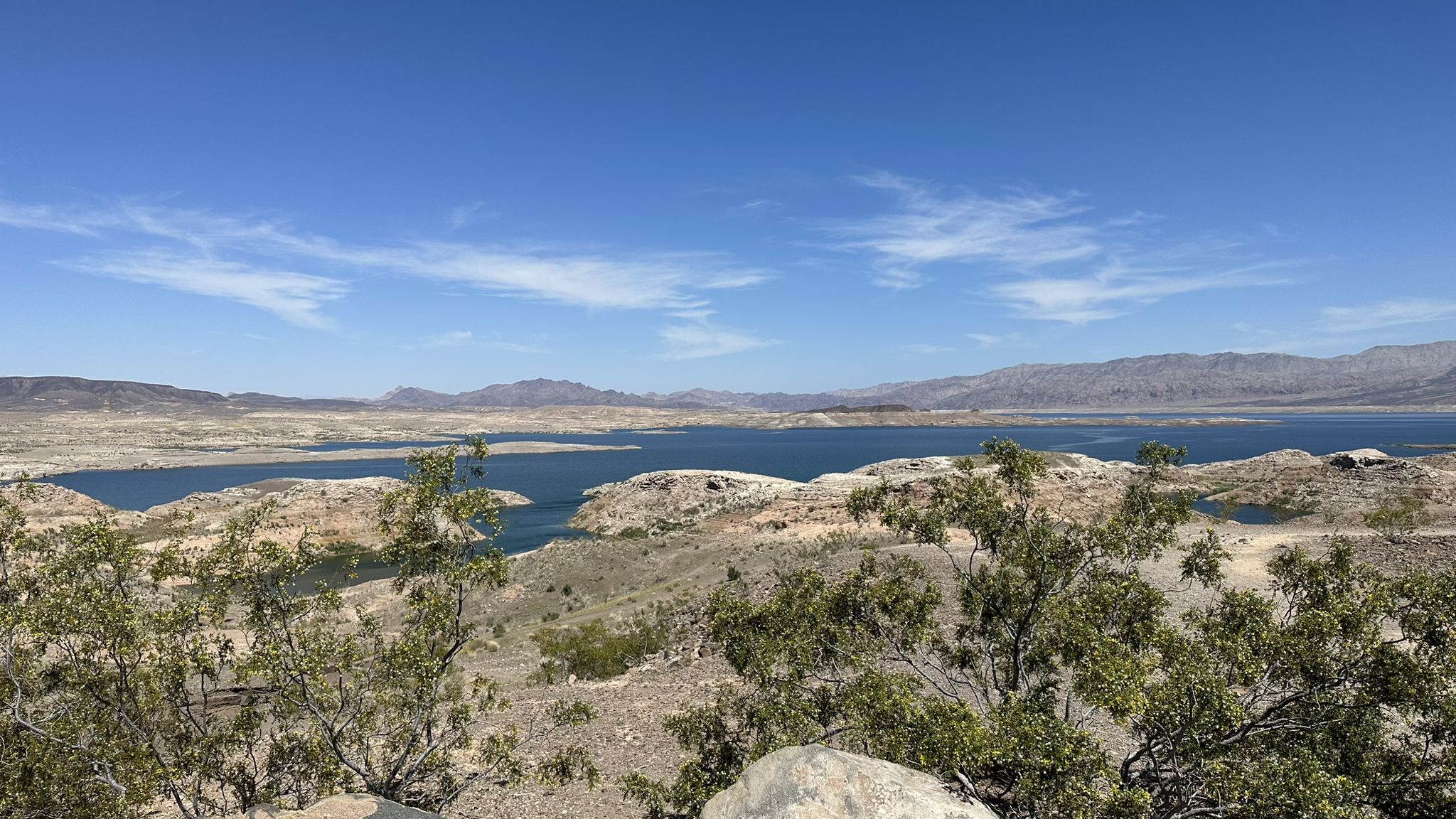 Panoramic view of a blue lake, rocky shores, and distant mountains. - Sunset View Scenic Overlook Trail