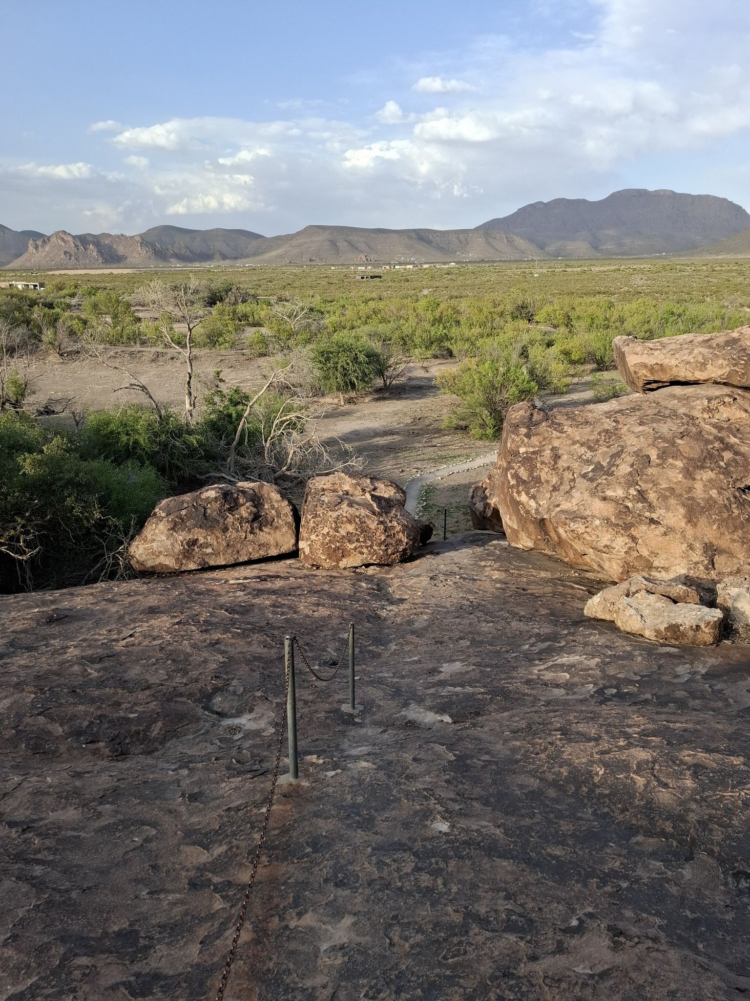 Rocky foreground with chain barrier overlooking a vast desert landscape and distant mountains. - Chain Trail