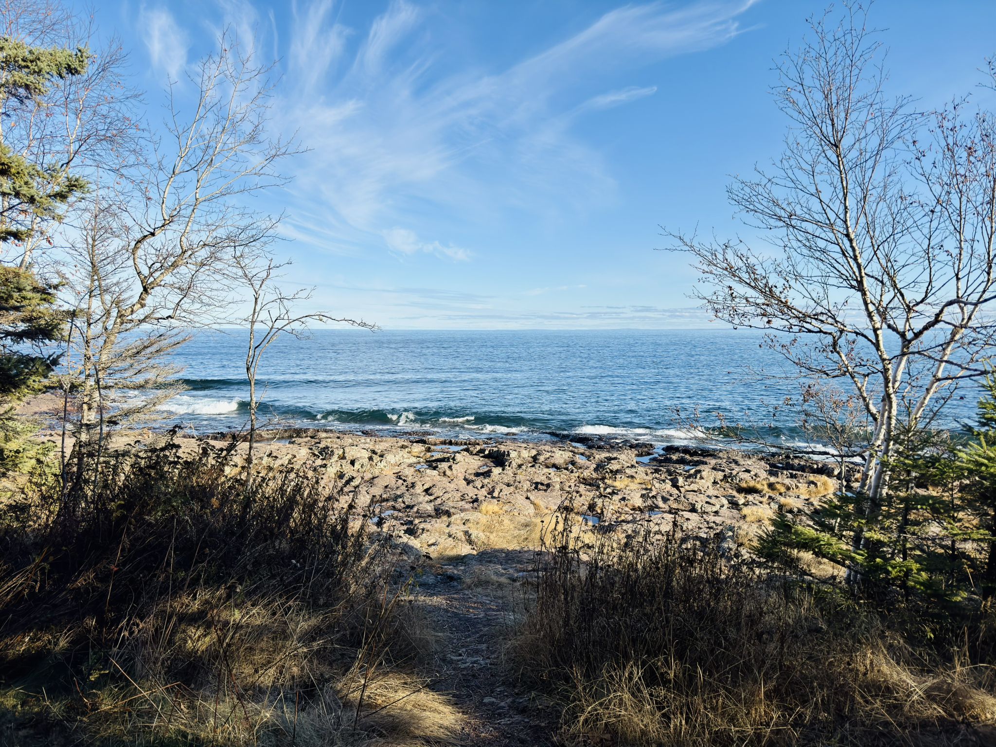 Rocky beach with waves, framed by bare trees under a bright blue sky. - Two Harbors Lighthouse