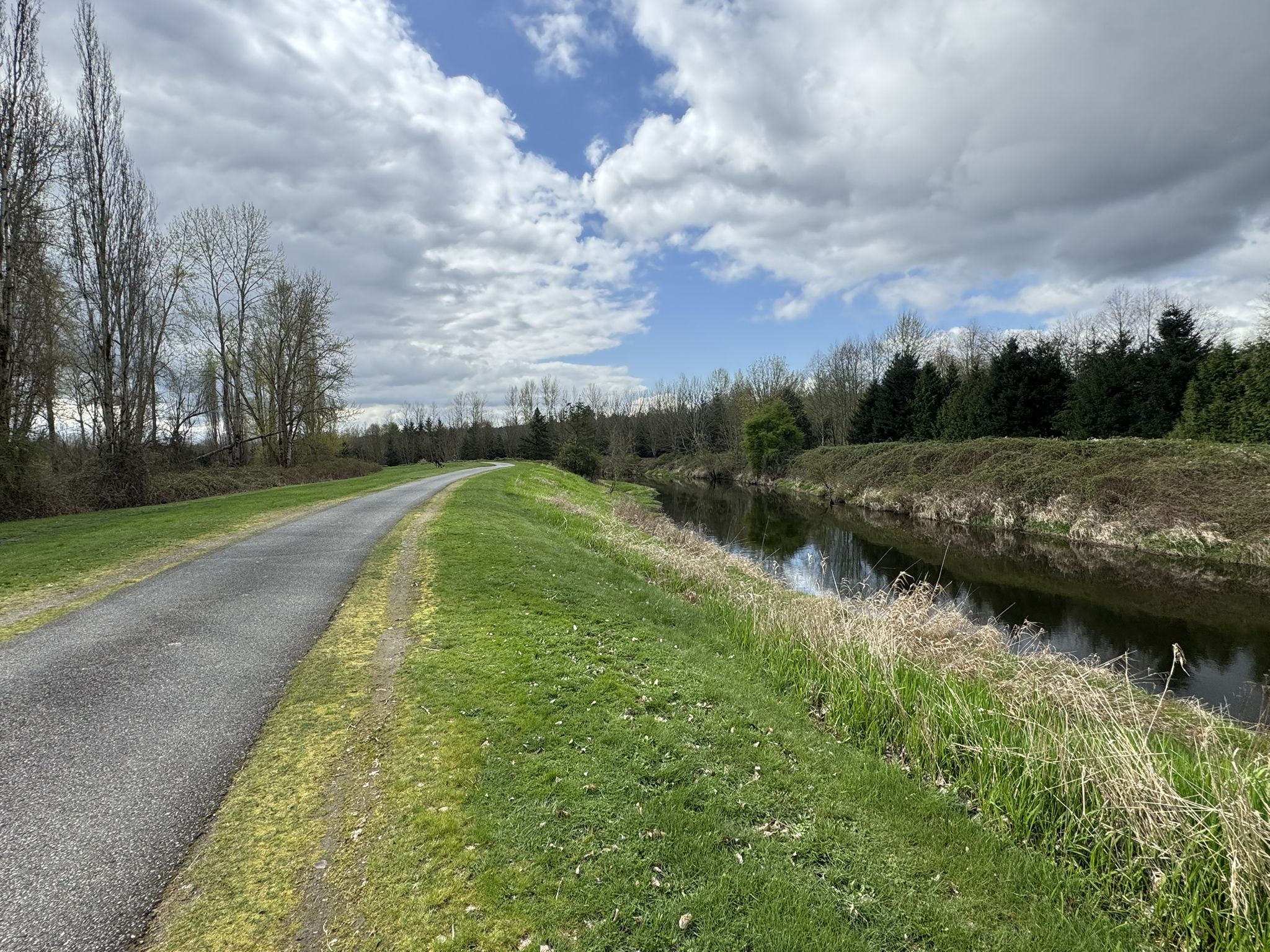 Paved path next to a river under a partly cloudy sky. - Lake Washington Loop