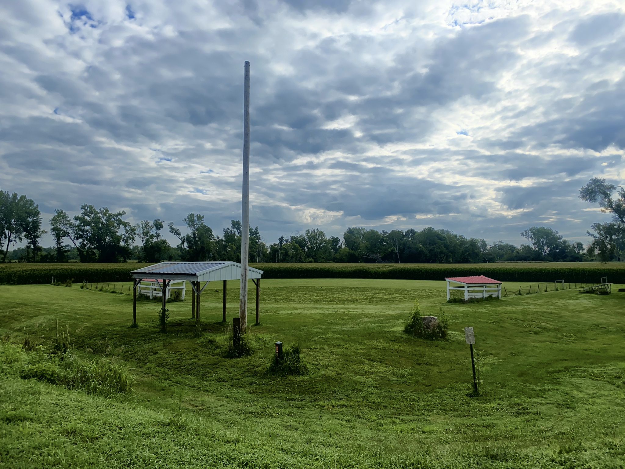 Grassy field with a tall pole and two small shelters under cloudy skies. - Chichaqua Valley Trail