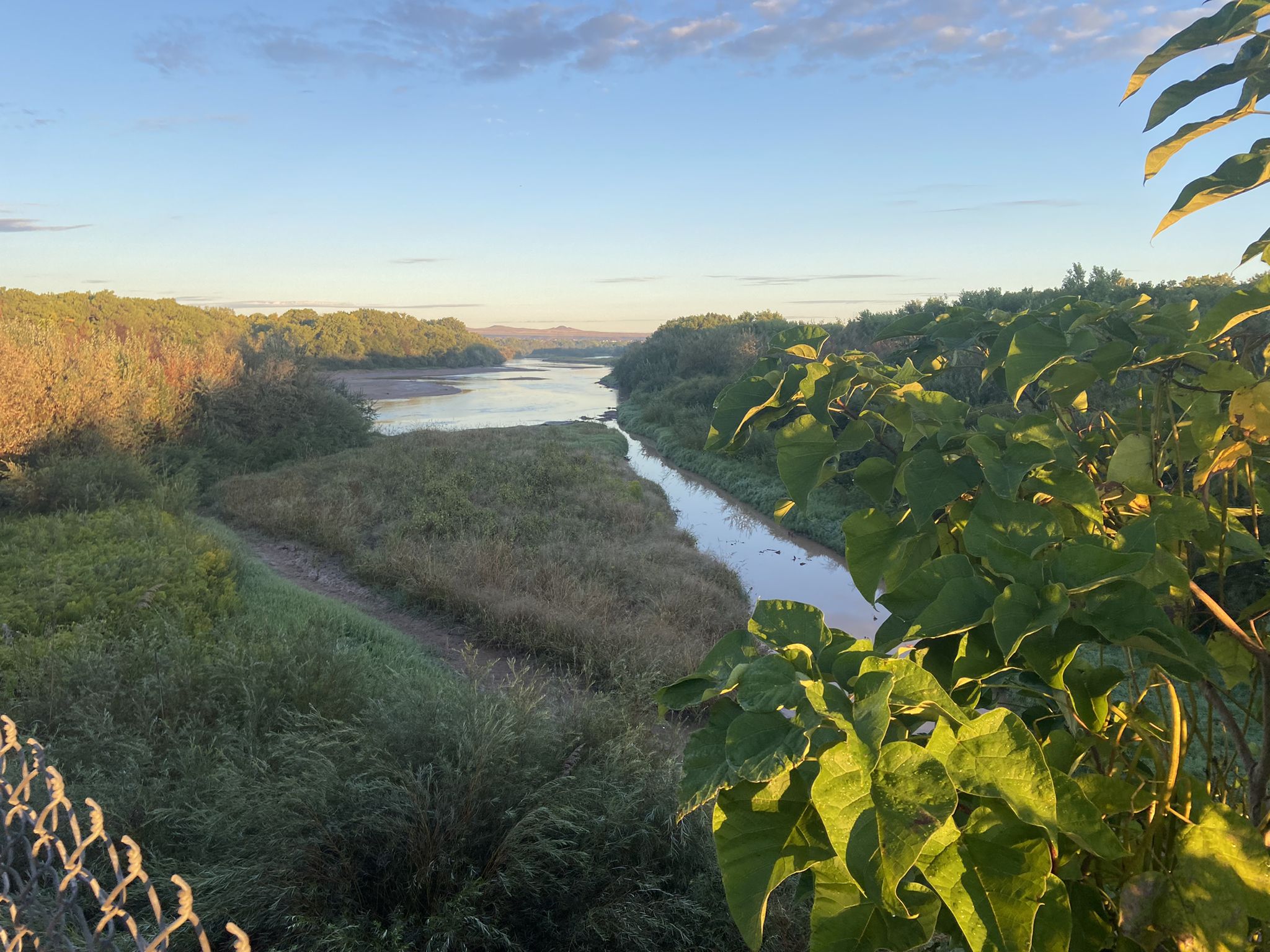 A winding river flows through a green valley at golden hour. - Atrisco Riverside Drain