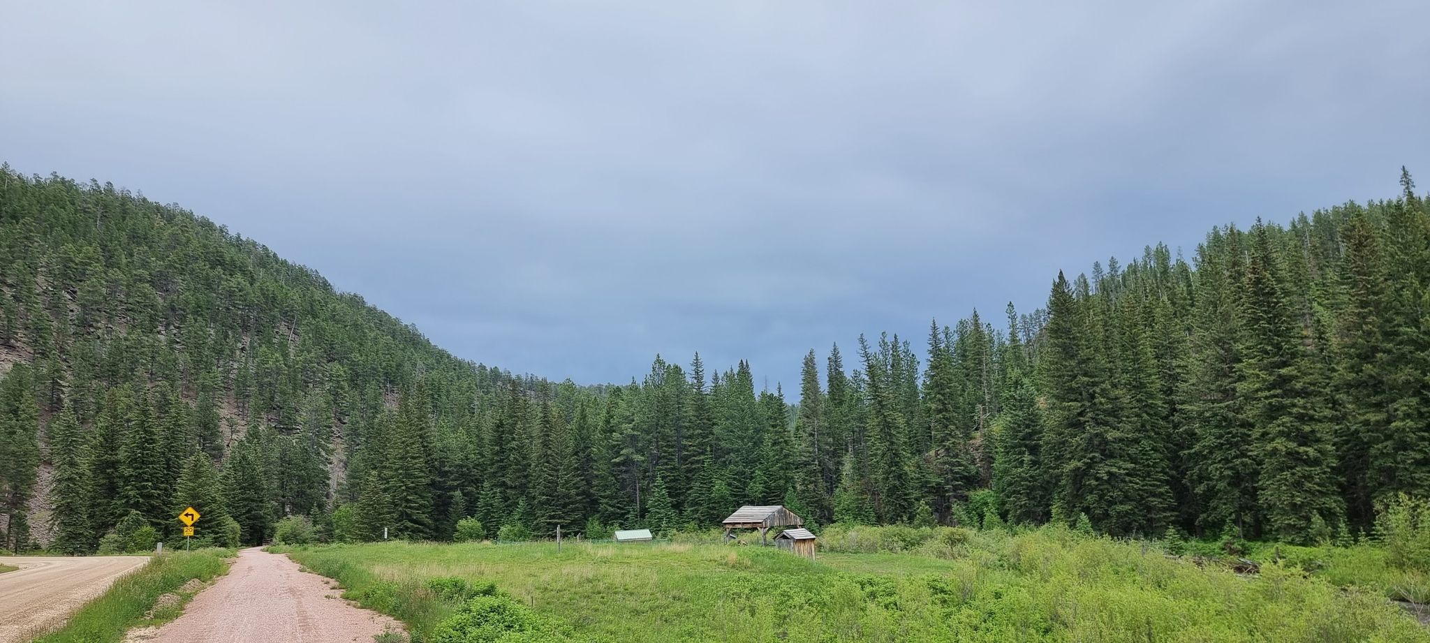 A small cabin in a green valley surrounded by dense pine forests under a cloudy sky. - Waterfall by Rochford Road – Bridge loop from Roubaix Lake
