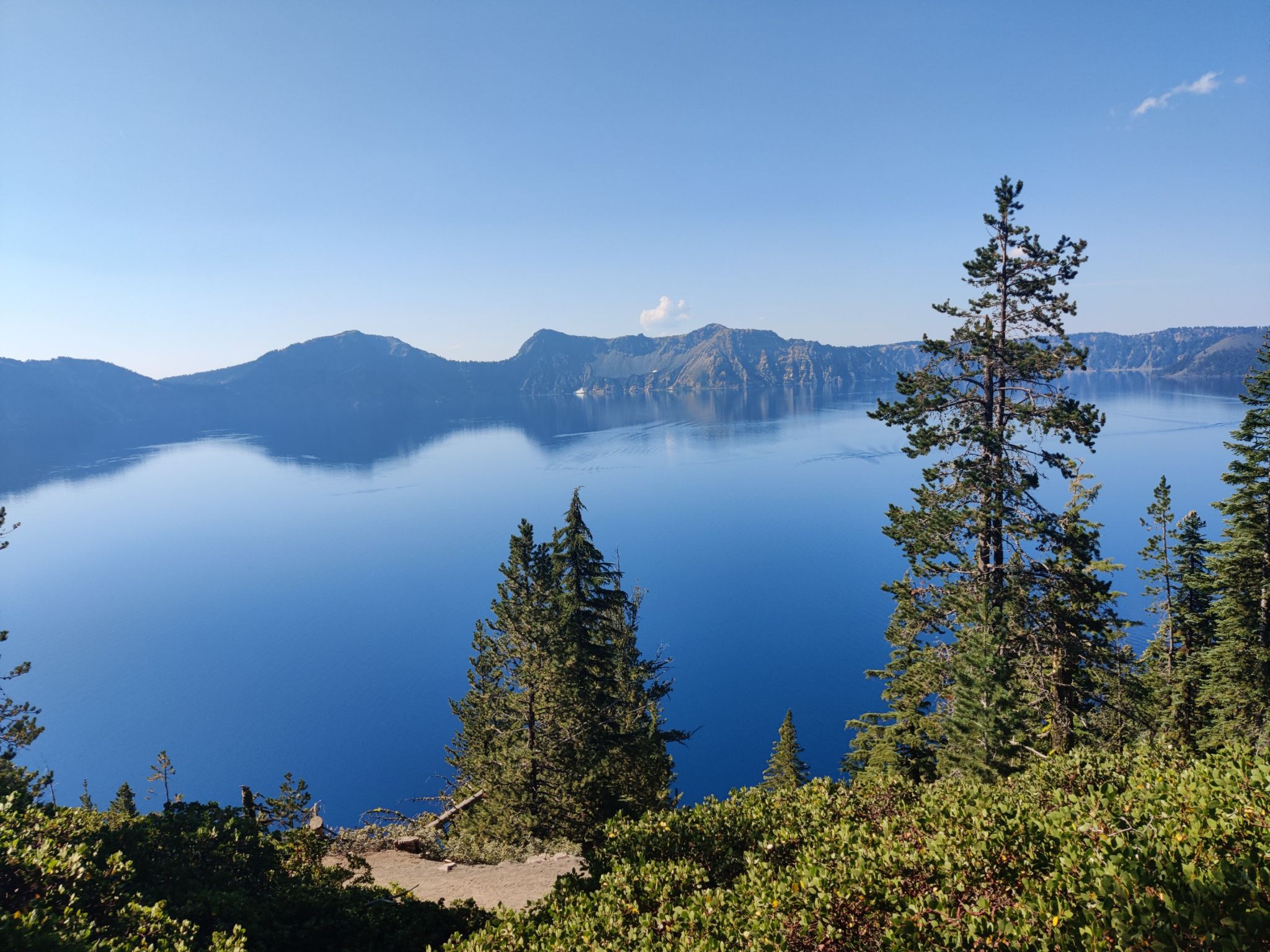 Vast deep blue lake surrounded by forested mountains under a clear sky. - Merriam Point to Cleetwood Cove