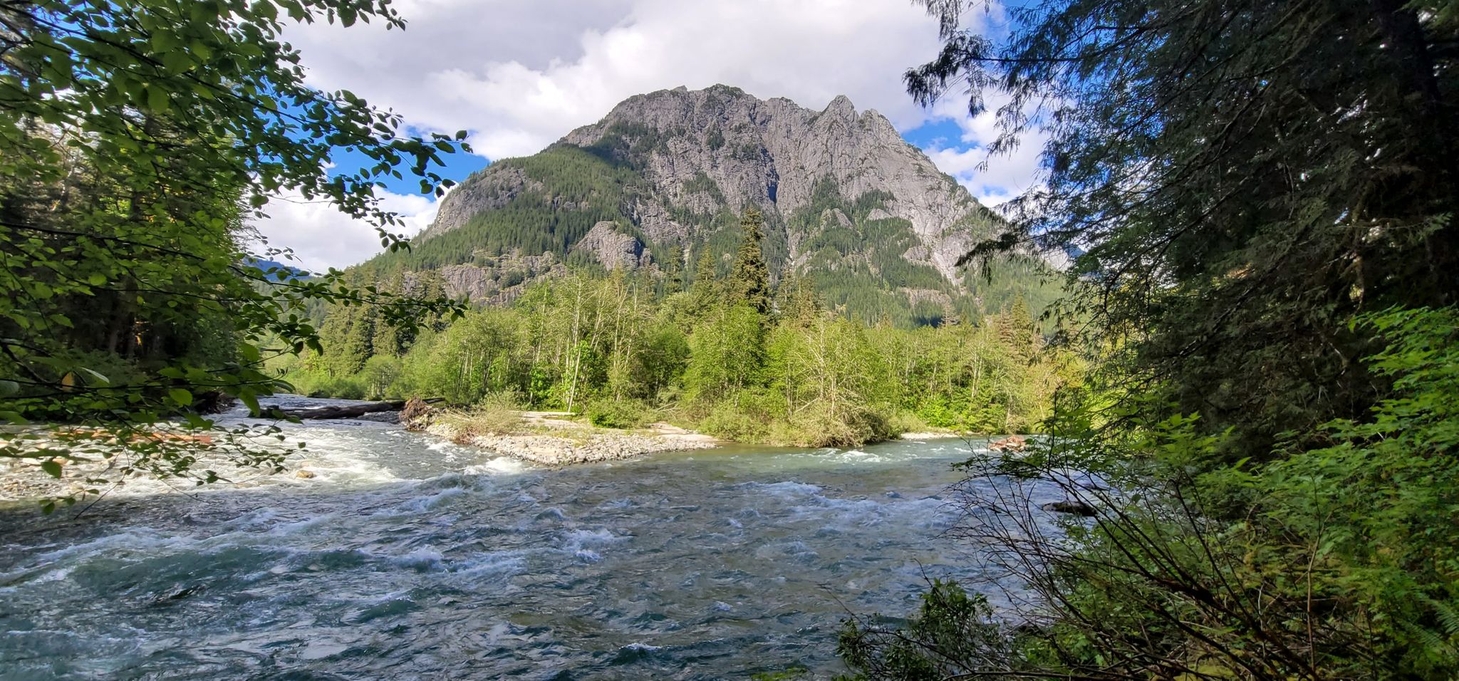 A wide river flows past a large forested mountain under a partly cloudy sky. - Middle Fork Snoqualmie River Trail