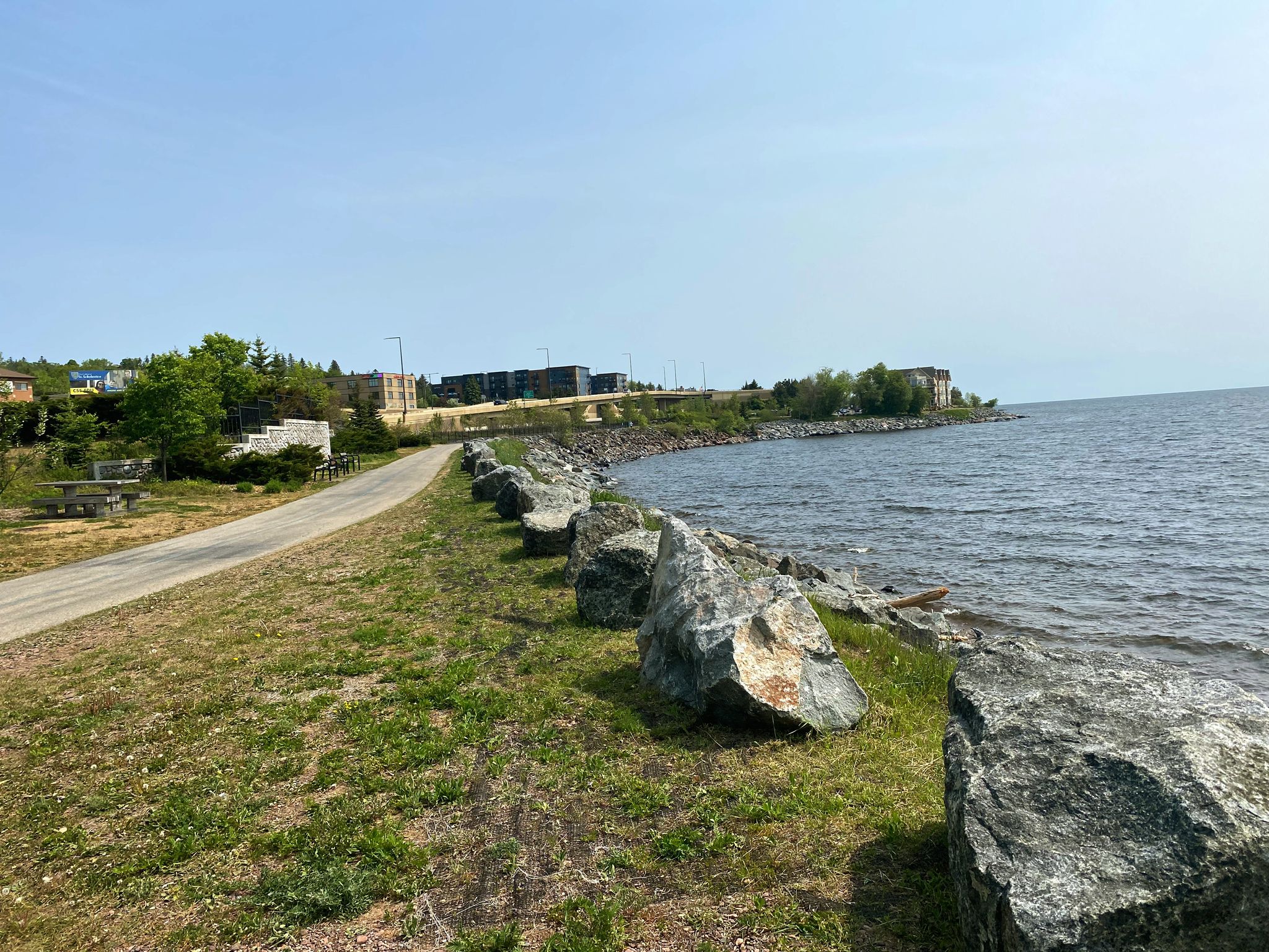 Paved path alongside large rocks and a calm body of water. - The Lakewalk