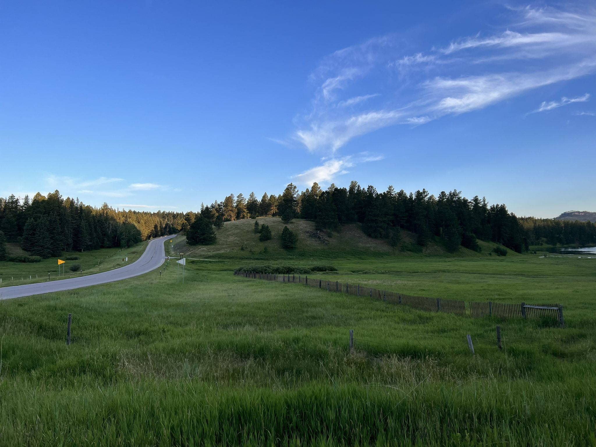 A winding road through green fields and a forest under a clear blue sky. - Deerfield Lake Loop Trail #40L