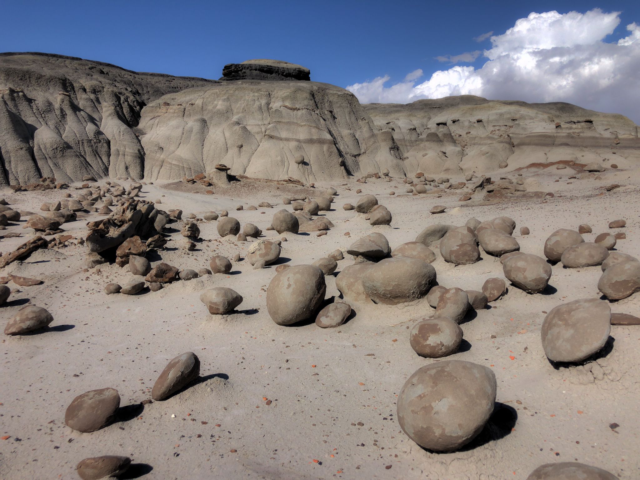 Many round boulders scattered across sandy ground with large rock formations behind. - Bisti Badlands Loop