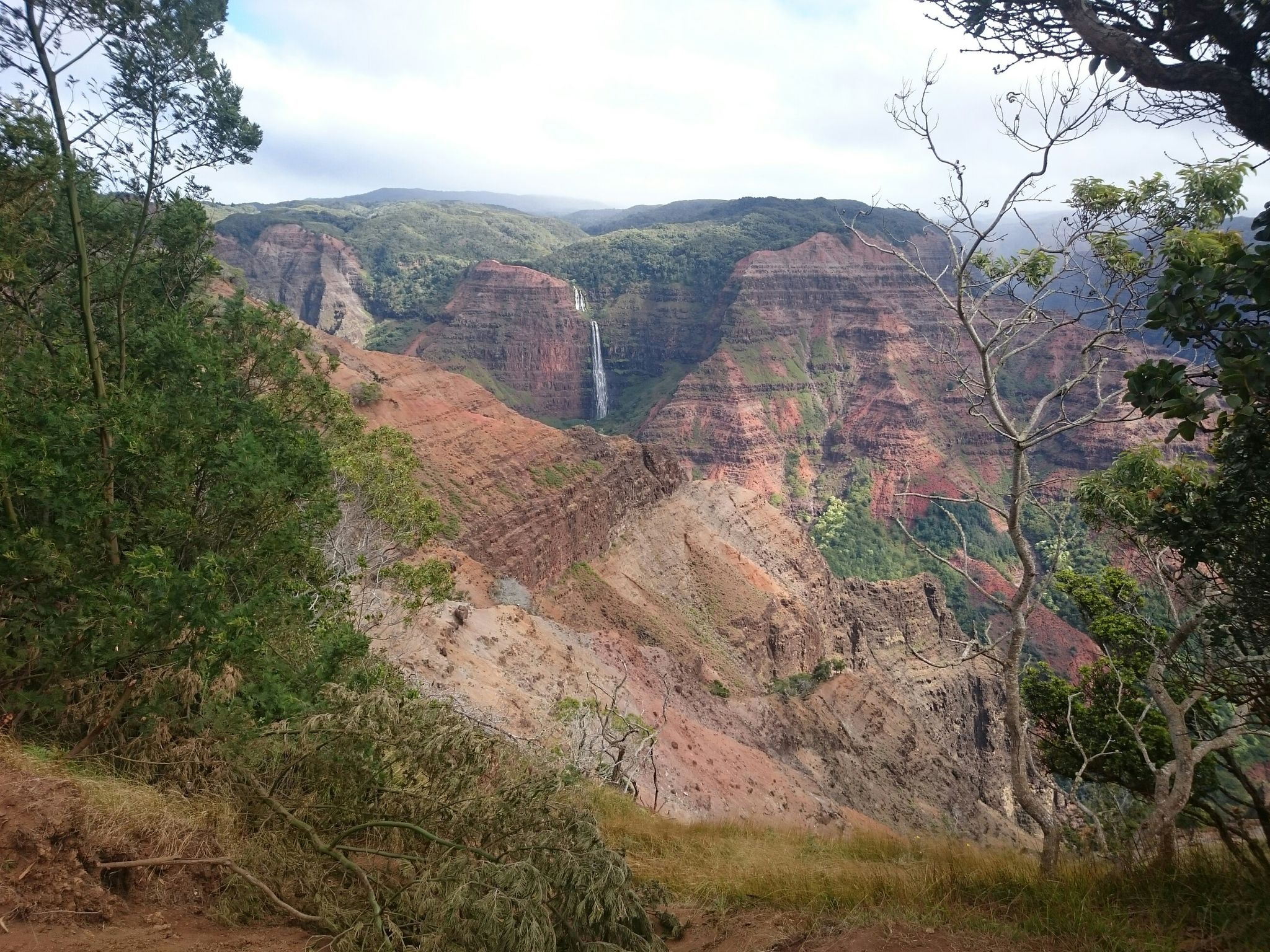 Tall waterfall cascades down a vast, colorful canyon under an overcast sky. - Highway 550