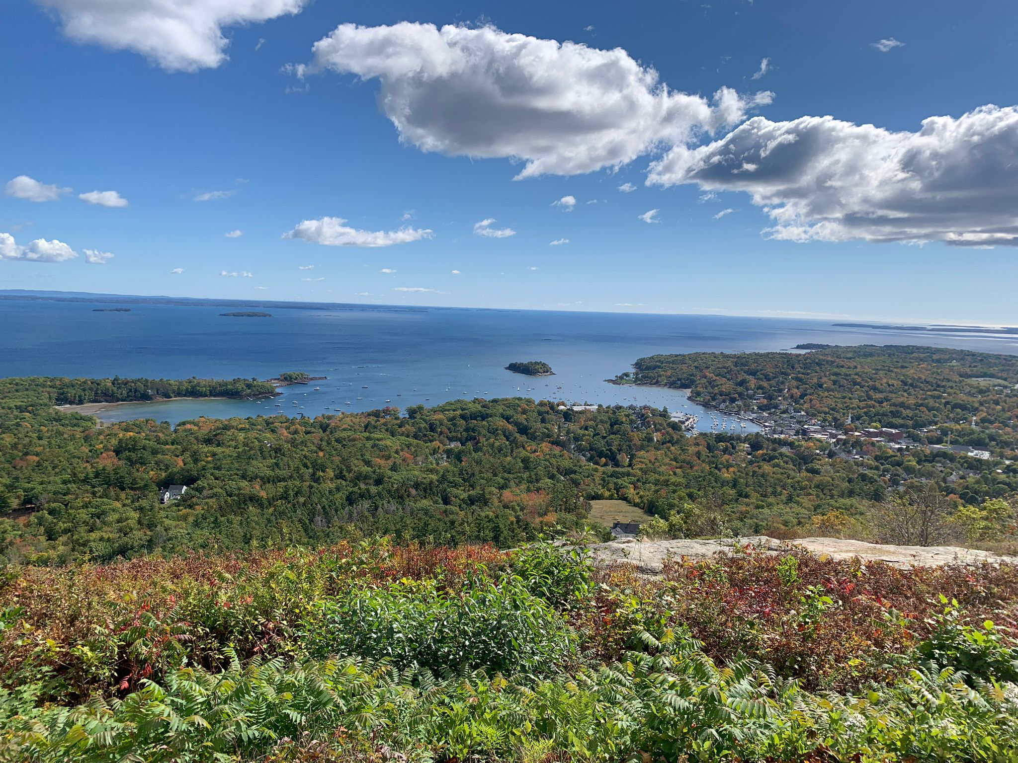 Expansive coastal view with islands, forested land, and a town under blue sky. - Mount Battie via Tablelands and Nature Trail