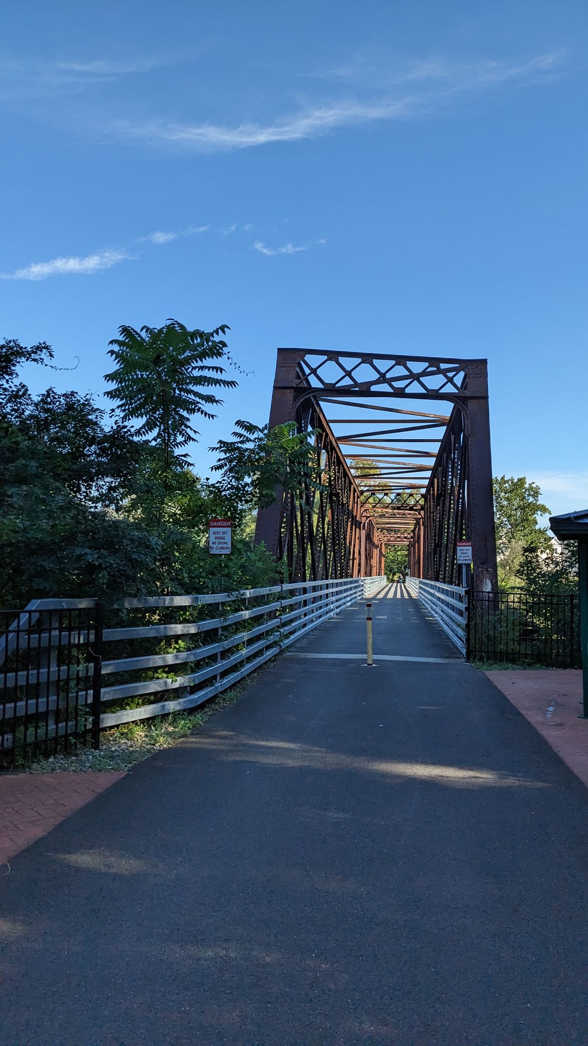 Paved path leading to a large metal truss bridge under a blue sky. - Empire State Trail fork loop from Cohoes