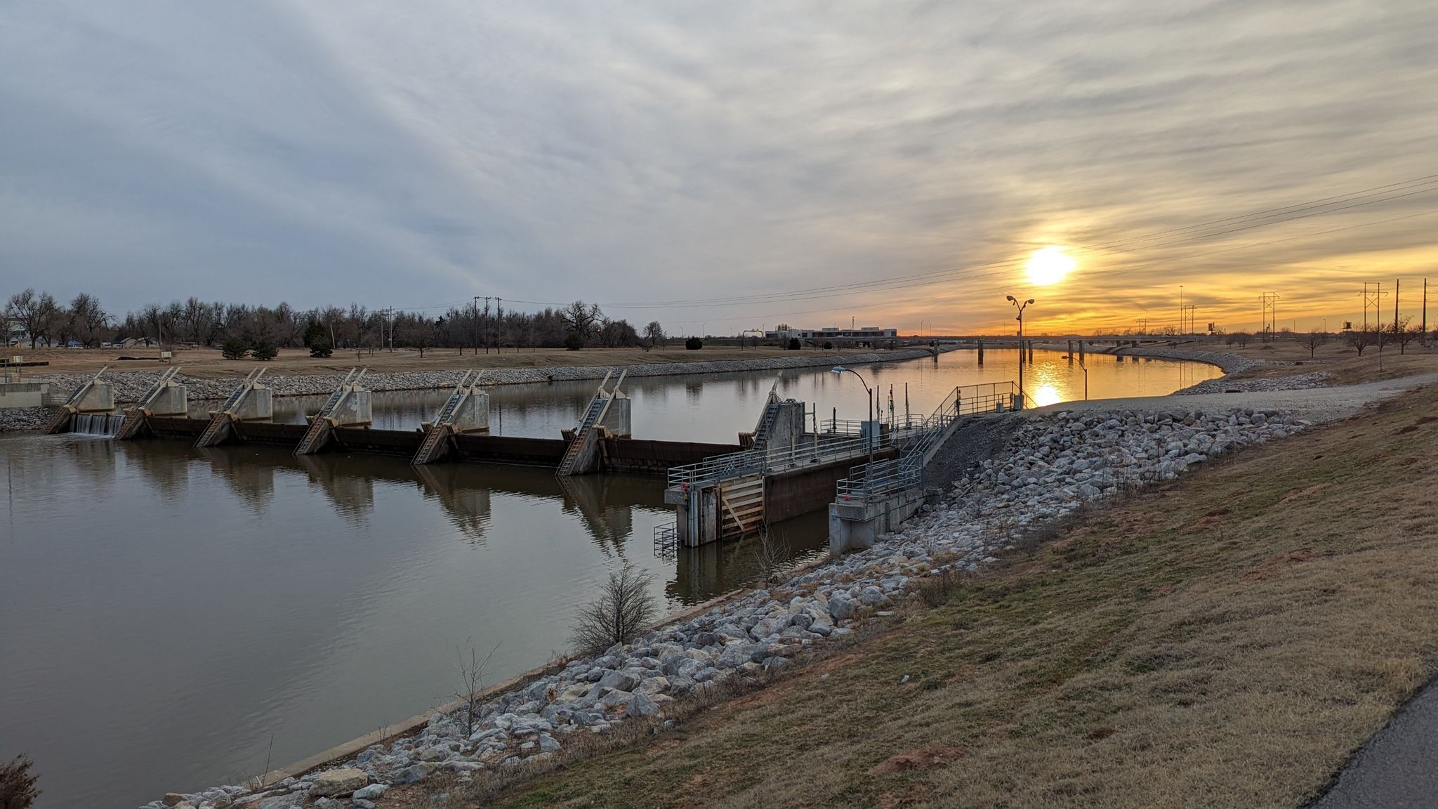 Sunset over a wide river with a dam and cloudy sky. - Oklahoma River Trail – Oklahoma River Trail - North loop from Hook & Reel