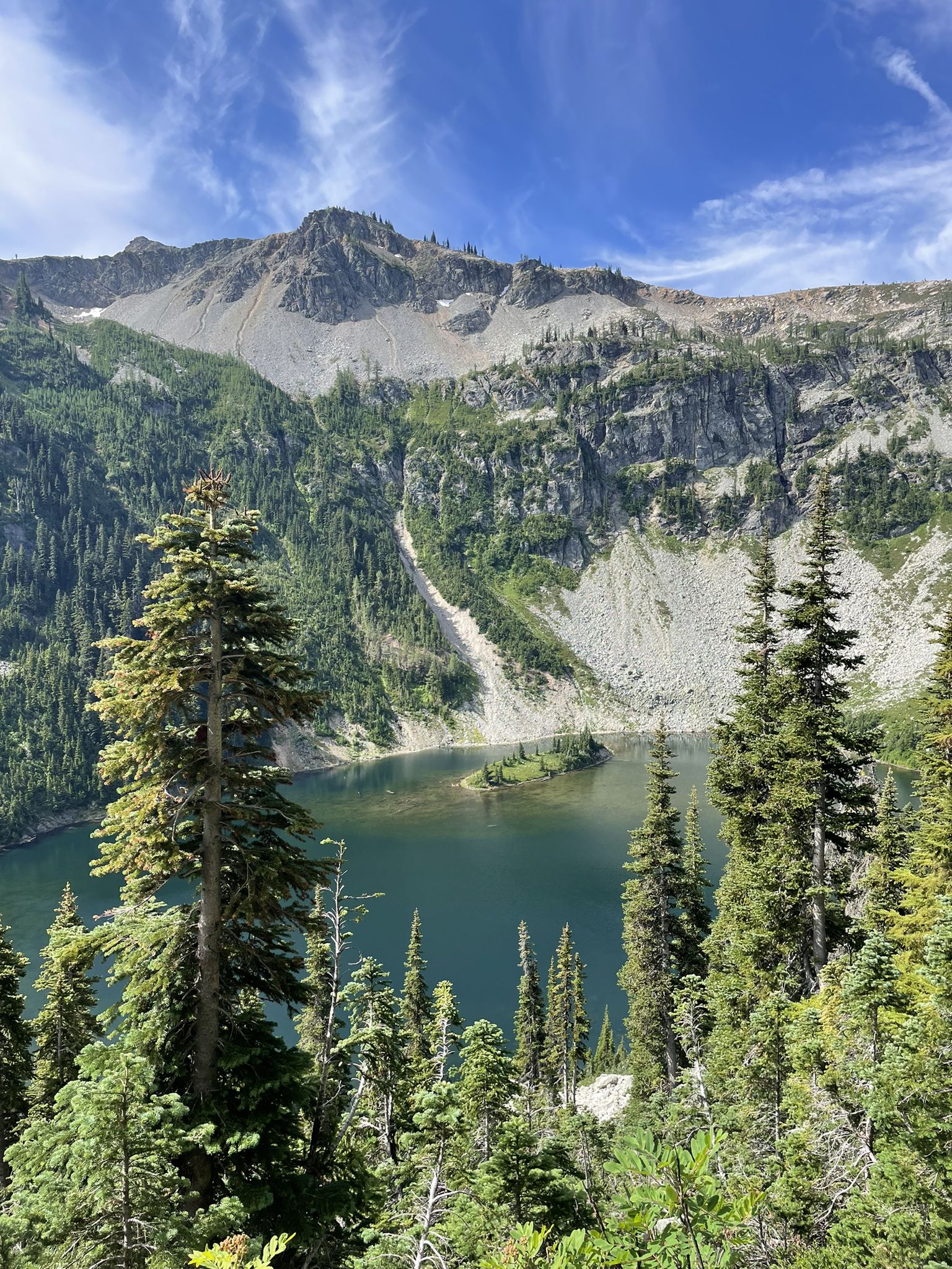 Mountain lake with an island, surrounded by pine trees under a blue sky. - Maple Pass Loop Trail