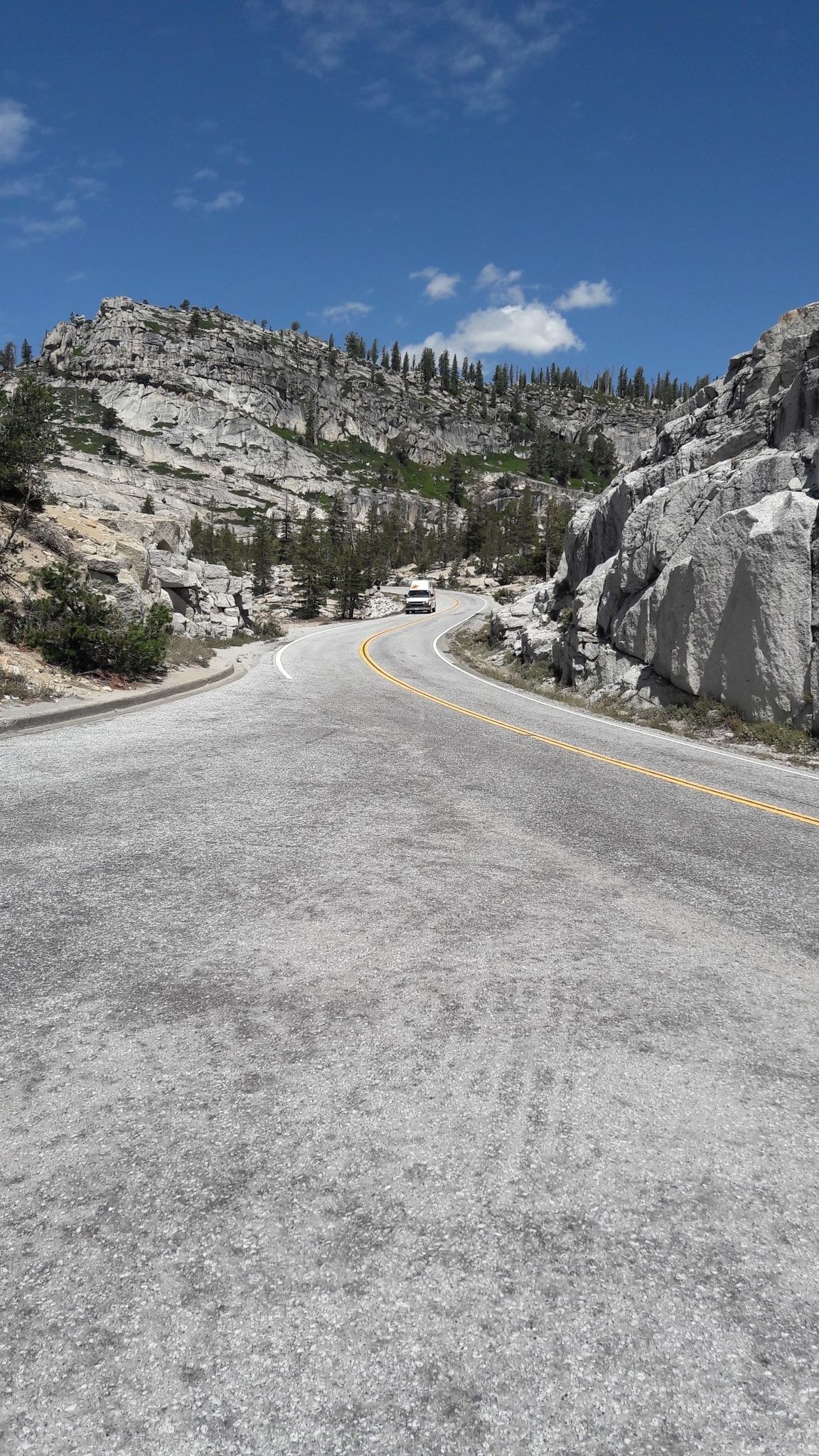 Winding mountain road through rocky terrain under a blue sky. - Tuolumne Grove of Giant Sequoias to Olmsted Point via Tioga Road
