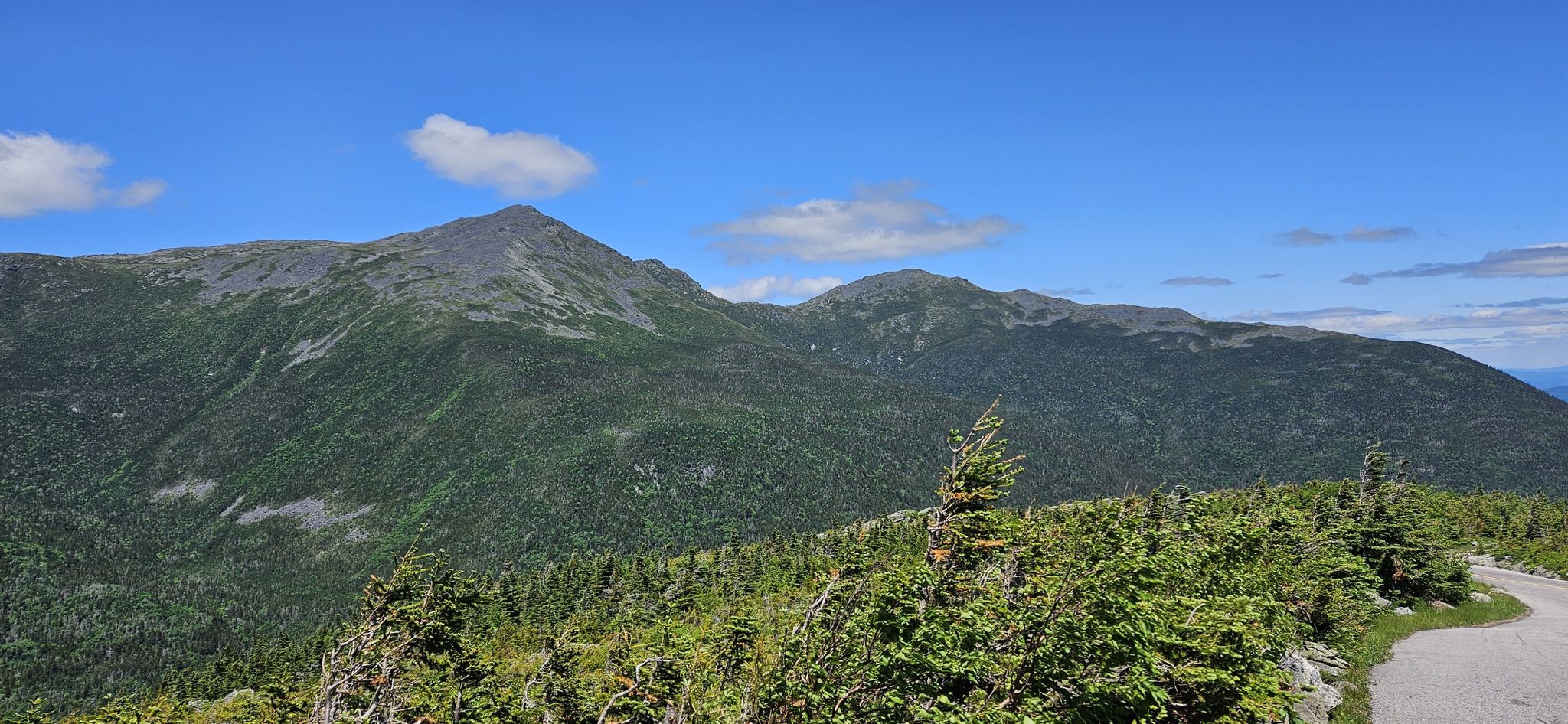 Lush green mountains and a winding road under a bright blue sky. - Mount Washington Auto Road Bicycle Hillclimb race course