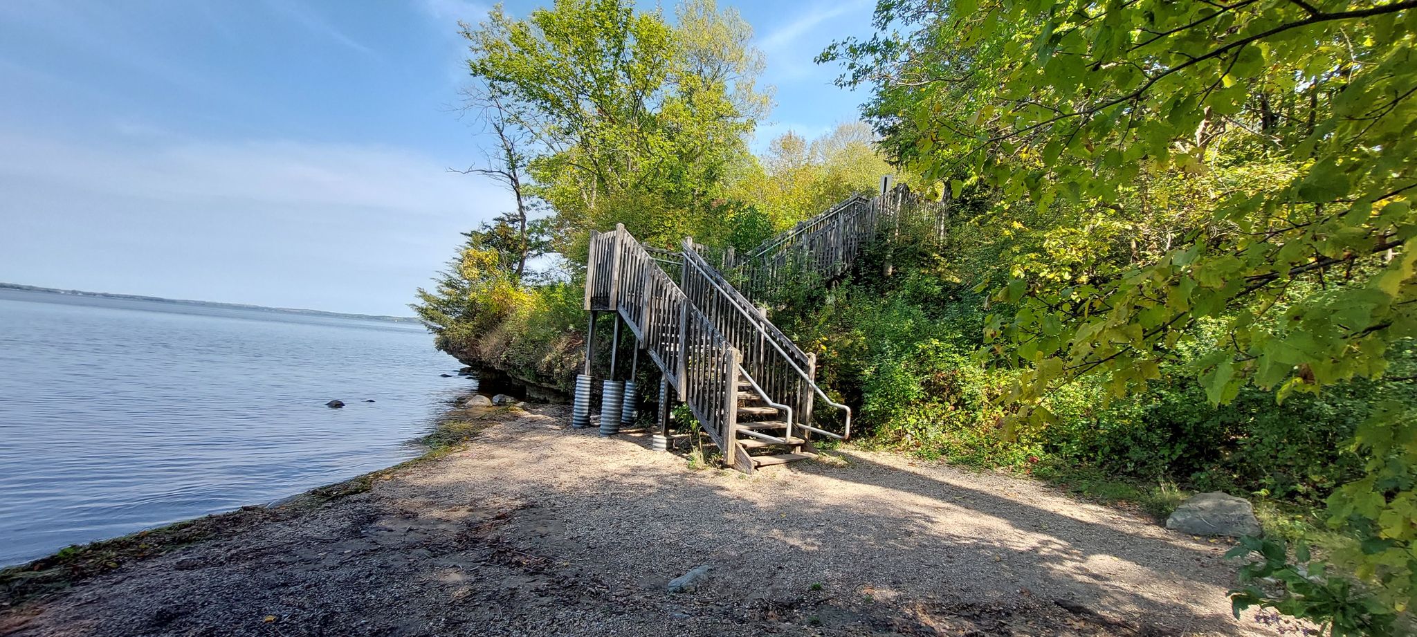 Wooden stairs ascend a tree-covered bank from a path by the water. - Raymer's Ravine and Eagle Heights Loop