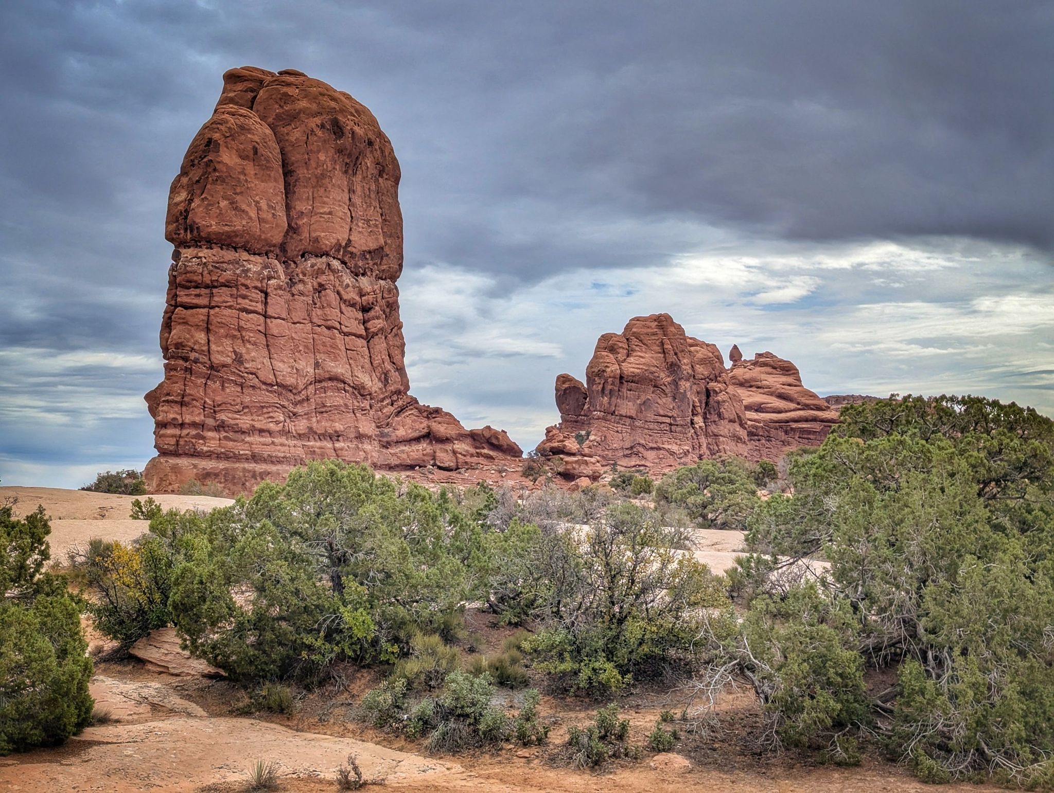 Large red rock formations stand tall under a cloudy sky in a desert landscape. - Willow Springs Road