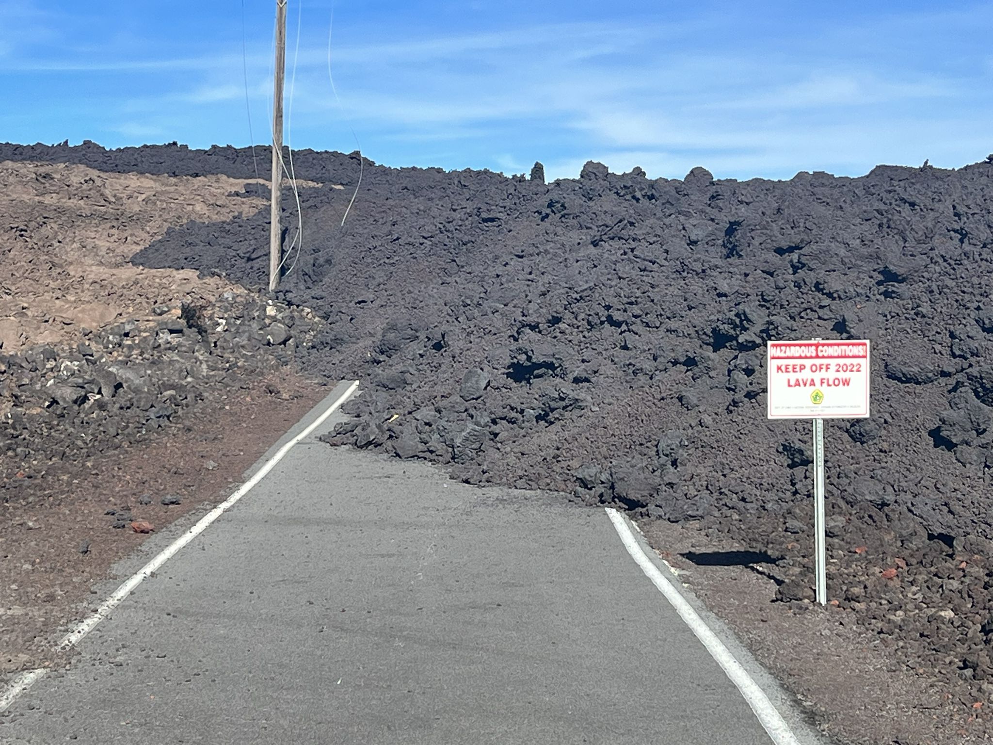 Road blocked by a massive dark lava flow under a clear blue sky. - Mauna Loa Observatory from Puʻu Huluhulu — Hawai‘i