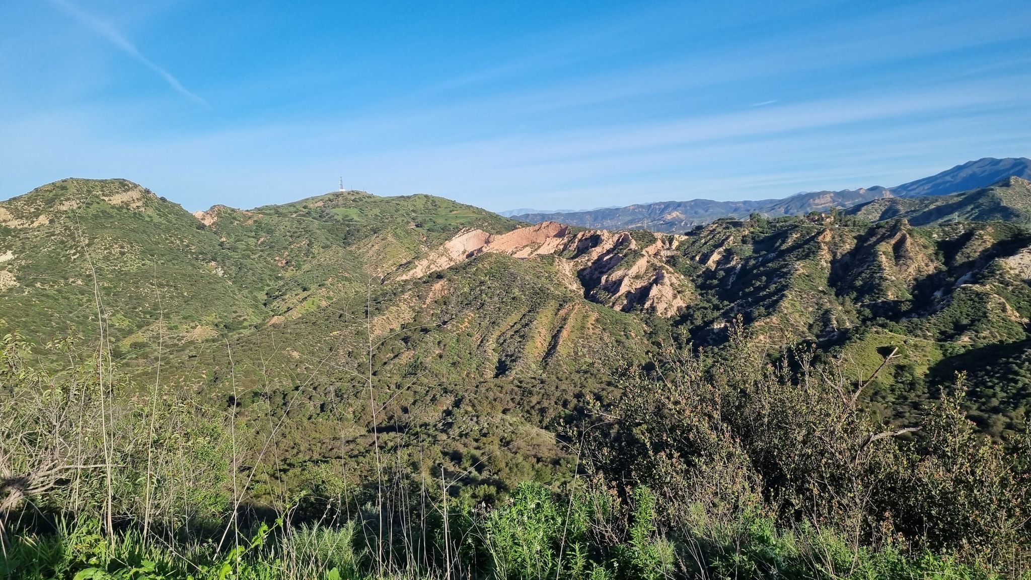 Green, rugged mountains with exposed rock formations under a clear blue sky. - Beginner Loop