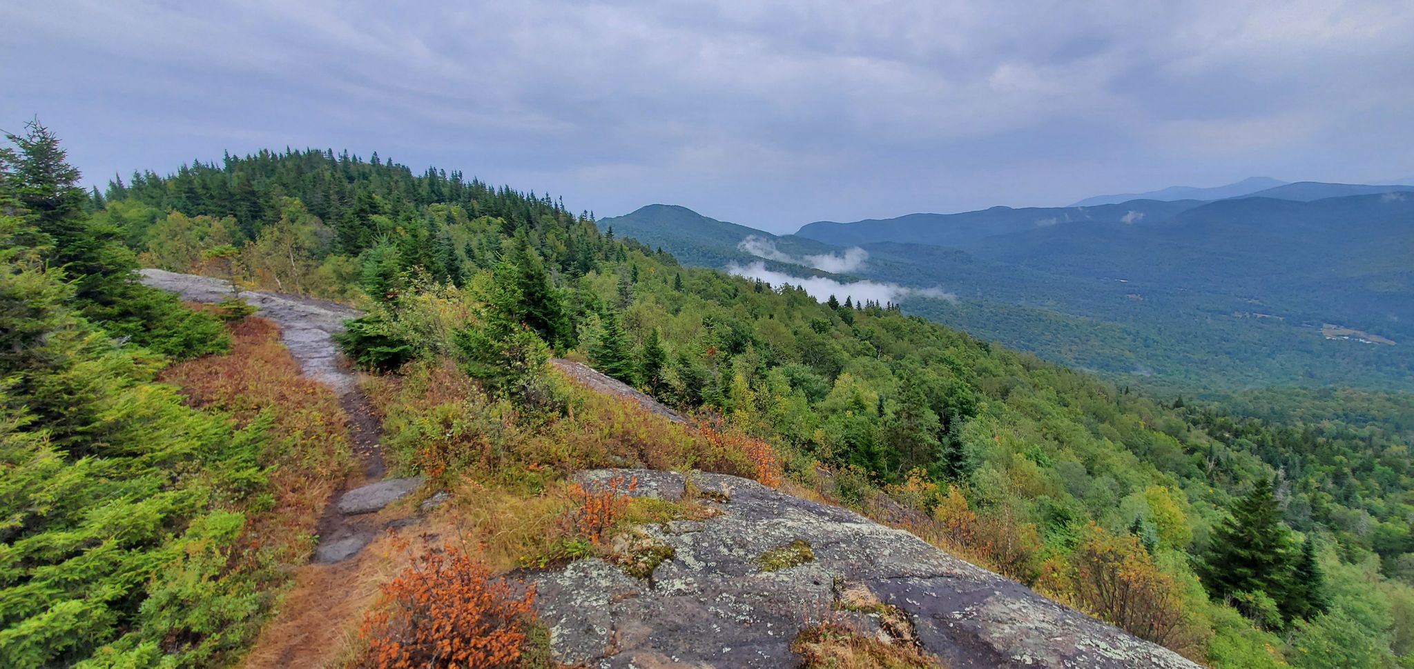 Overcast view from a rocky mountain outcrop overlooking a forested valley. - Jay Mountain Trail